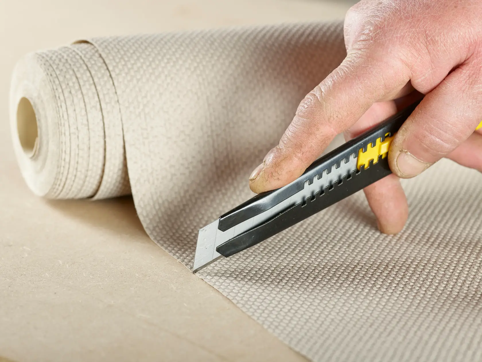 Photo of STANLEY 0-11-301 utility knife cutting textured material roll, close-up, product photography.