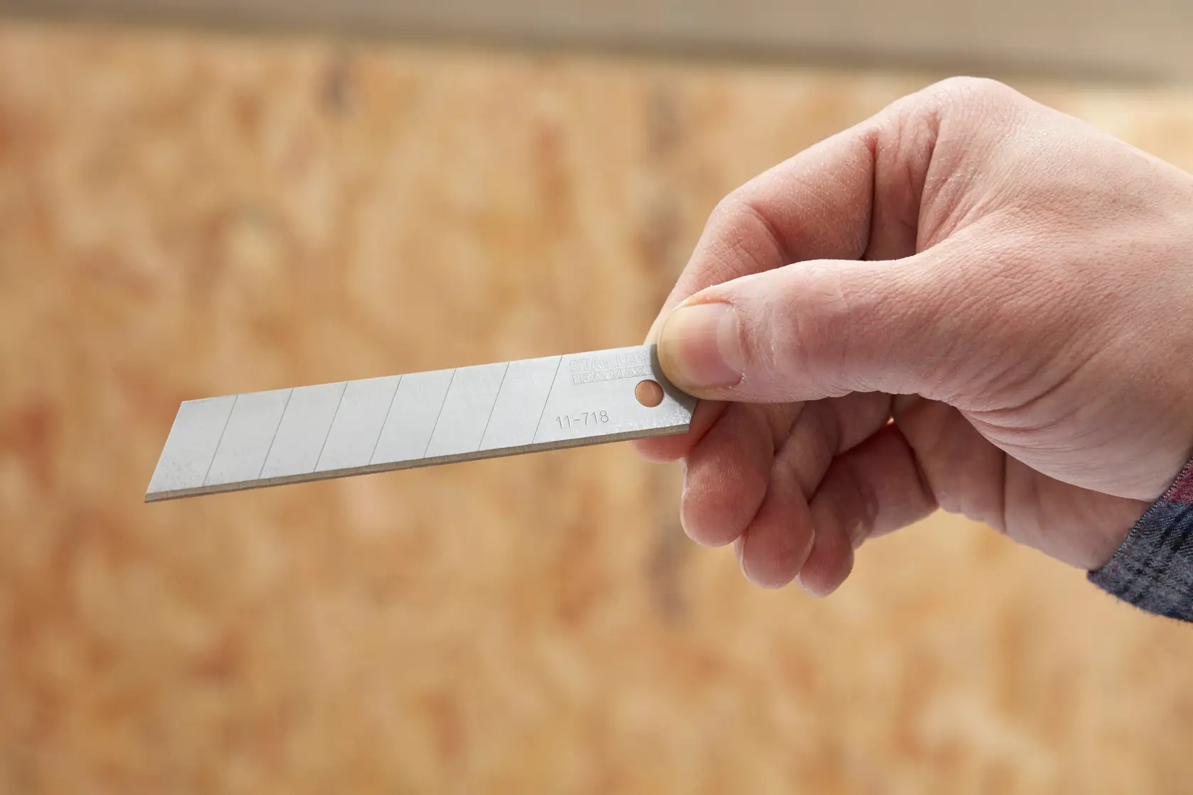 Photo of a hand holding a STANLEY 0-11-718 snap-off utility blade, close-up view.