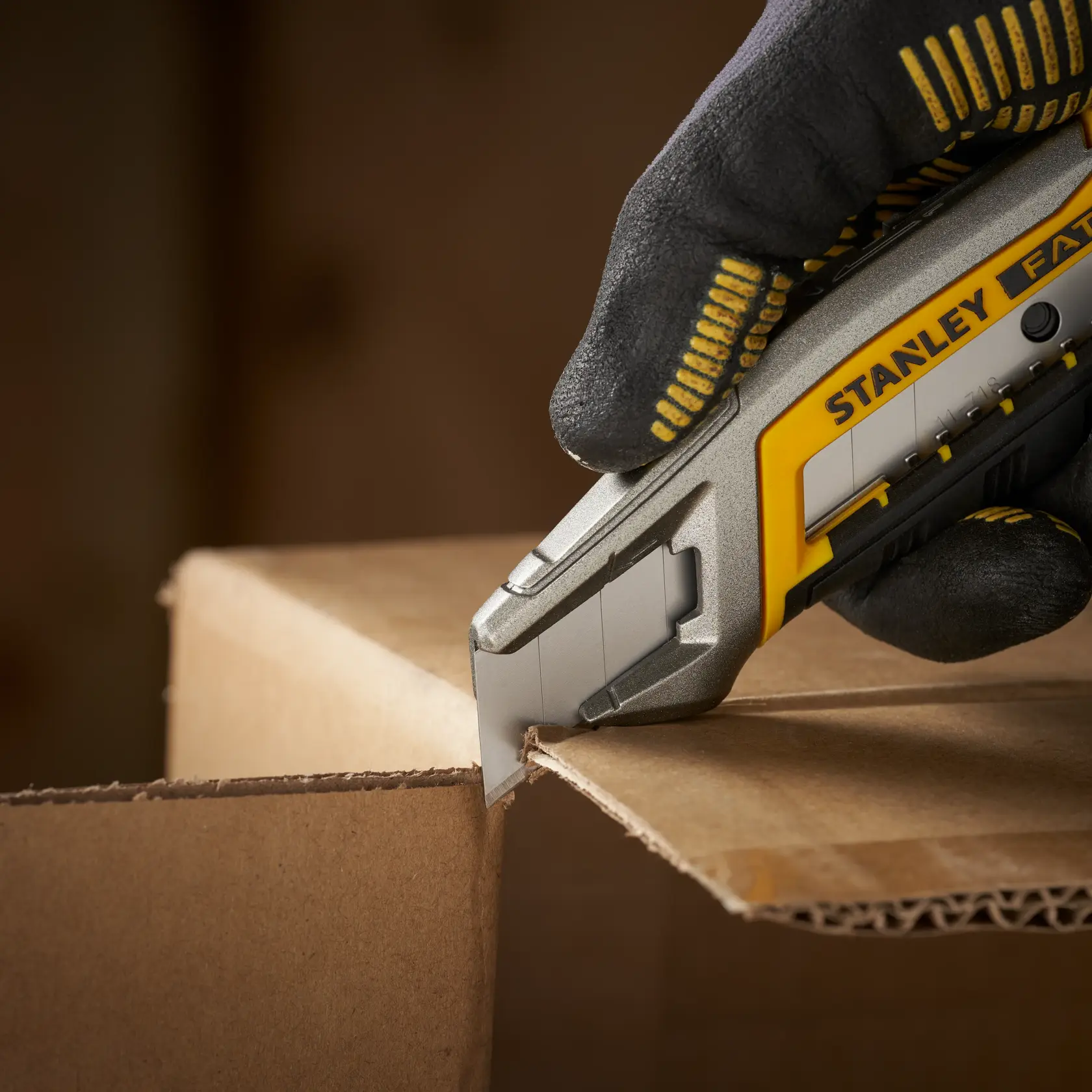 STANLEY 0-11-718 utility knife cutting cardboard, close-up photo showing gloved hand and blade.