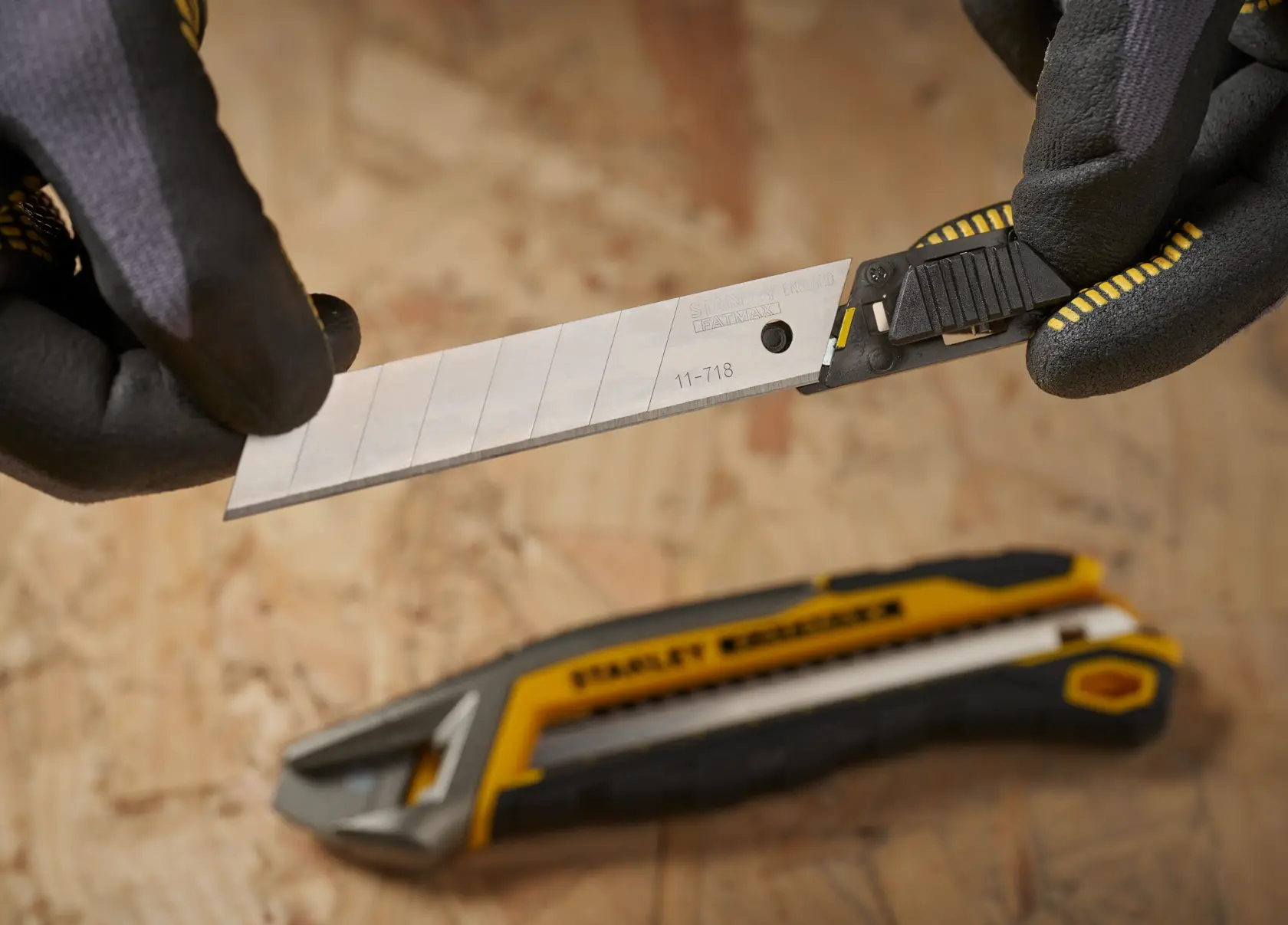 STANLEY 0-11-718 snap-off utility blade held in gloved hands, yellow and black knife in background.