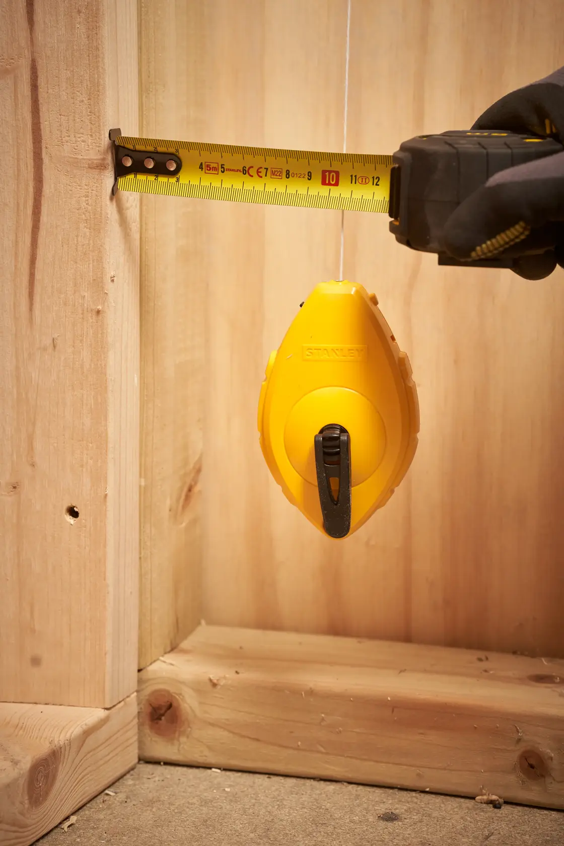 STANLEY 0-47-440 chalk line reel in use with measuring tape near wooden framing, close-up.