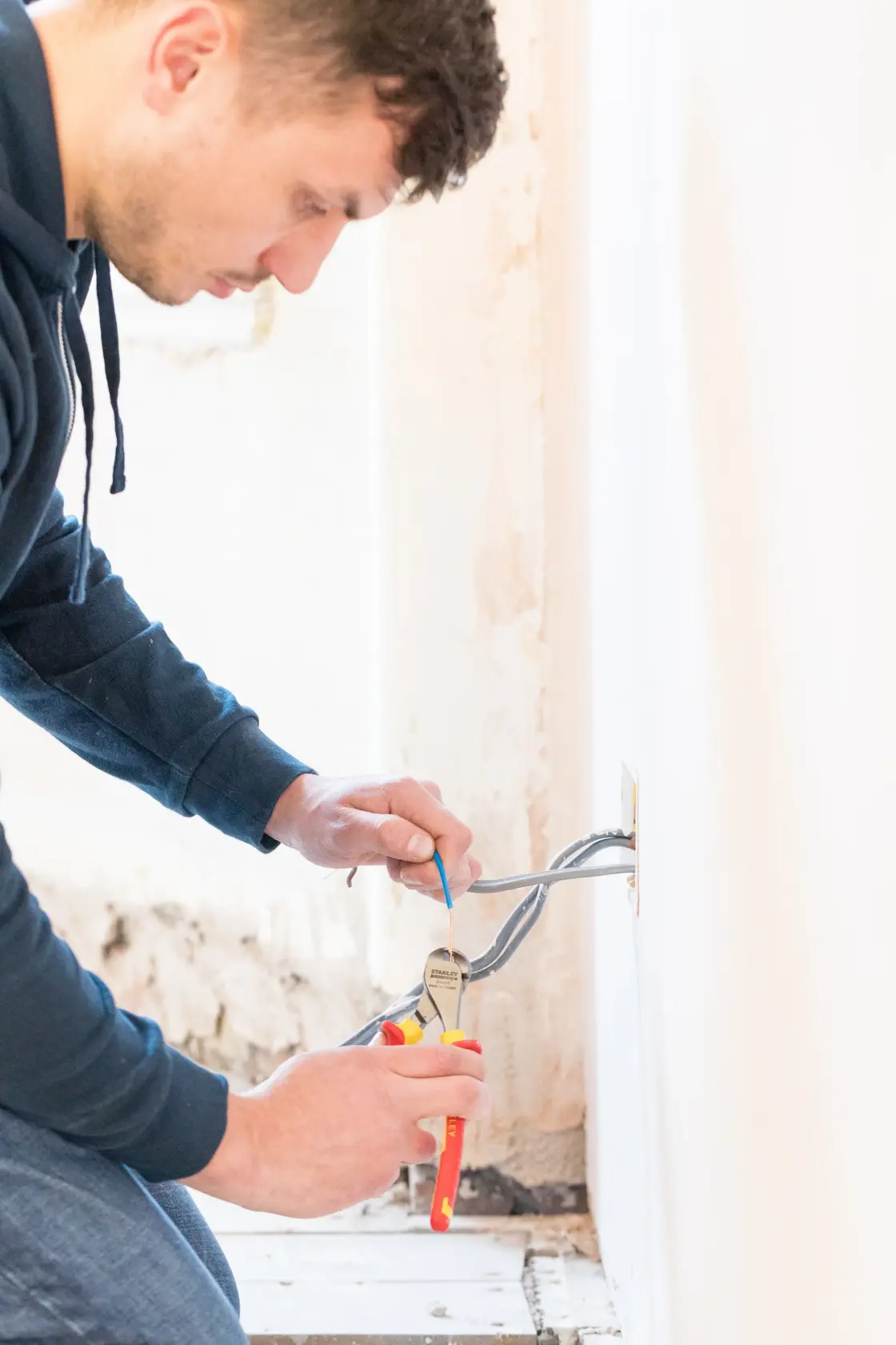 Photo of STANLEY 0-84-016 pliers used for electrical wiring repair near a wall outlet.