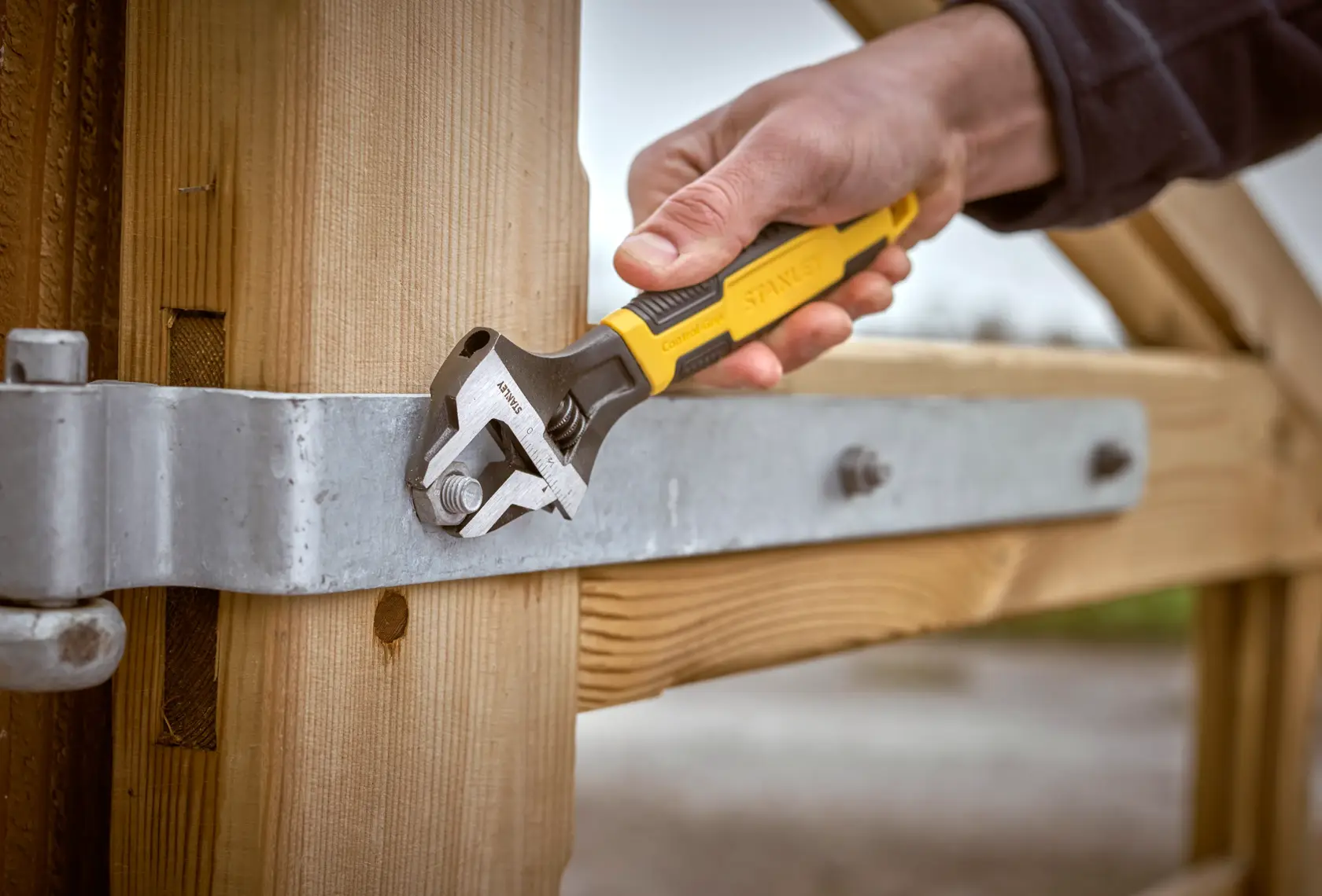 STANLEY 0-90-947 adjustable wrench used on metal bolt, close-up photo, hand-held tool on wooden gate.
