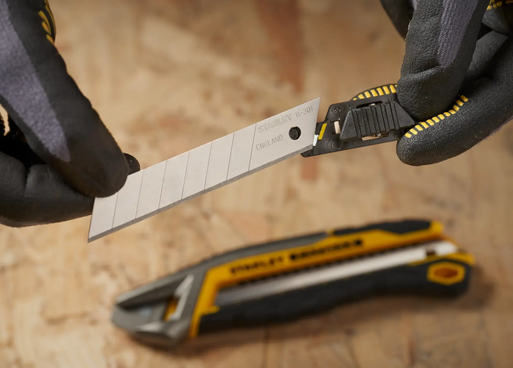 STANLEY 1-11-301 utility knife blade close-up, held by gloved hands, cutter on wood background.