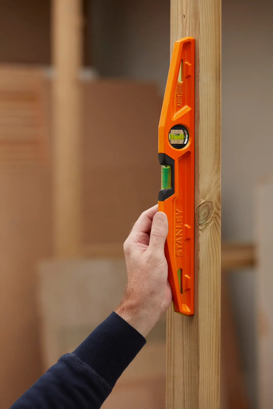 STANLEY 1-42-312 orange spirit level held vertically against wooden beam, photography.