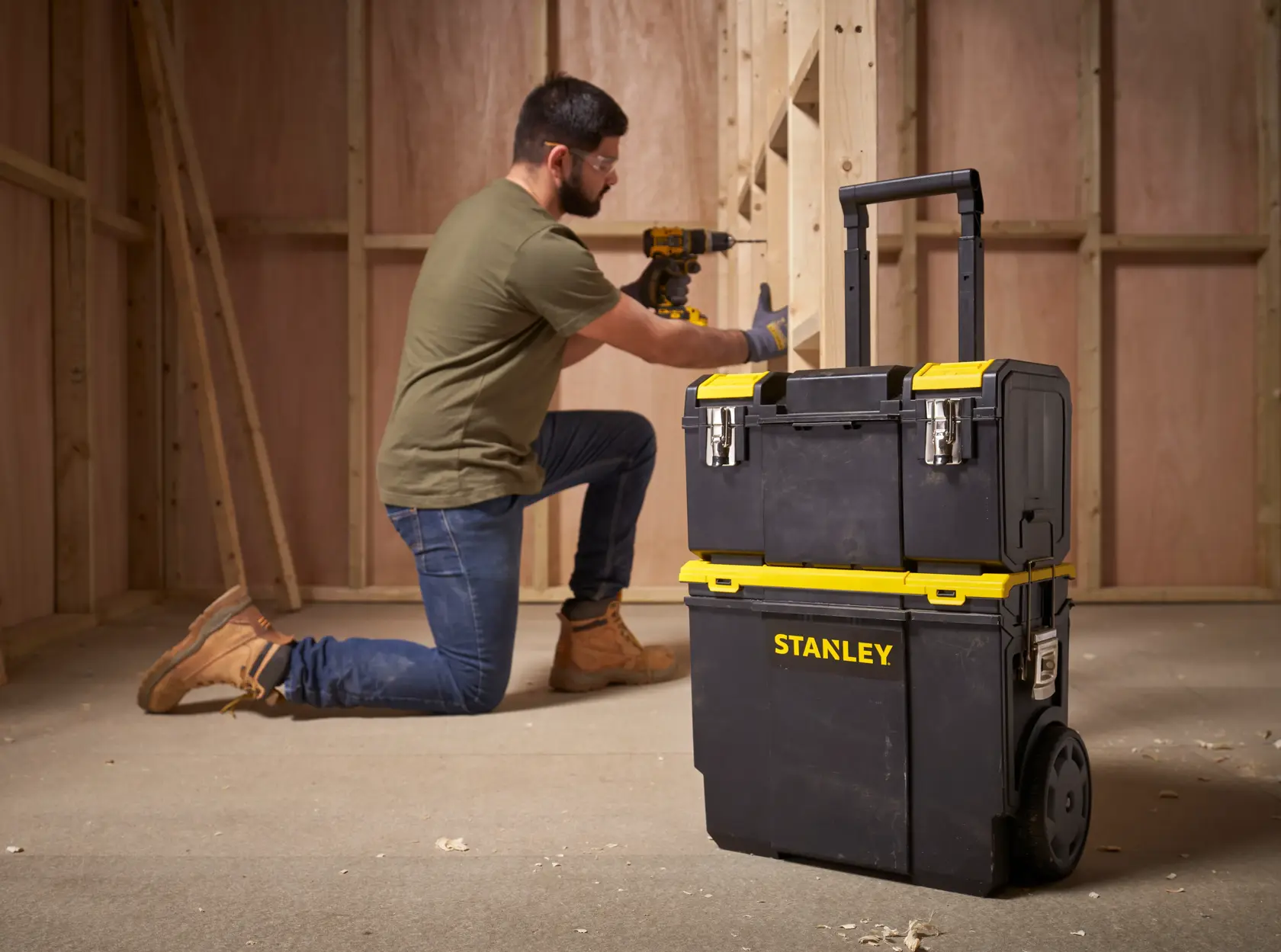 Photo of STANLEY 1-70-326 rolling tool box with yellow accents, shown on jobsite with worker in background.