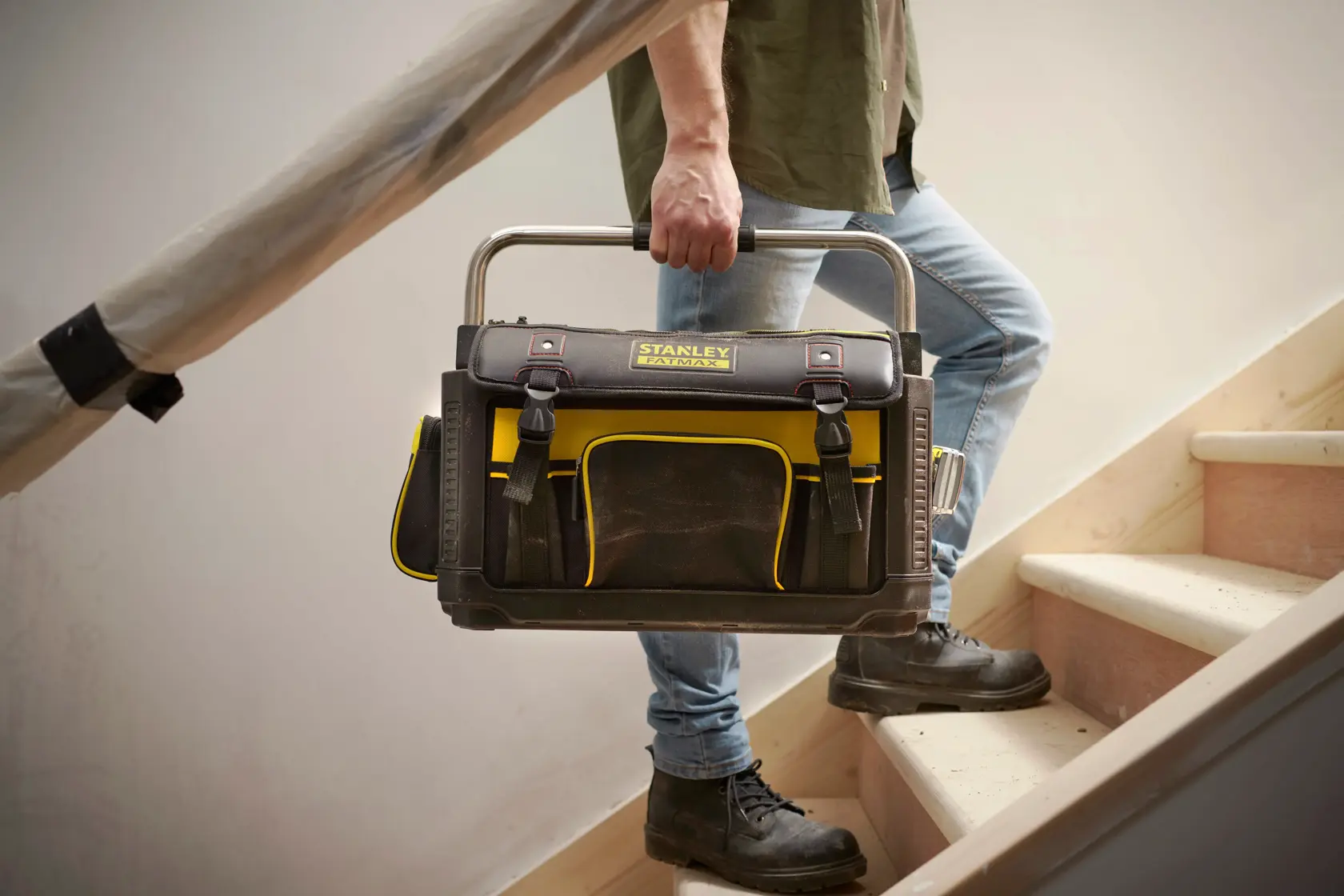 STANLEY 1-79-213 tool bag in black and yellow, photographed being carried up stairs by a person.