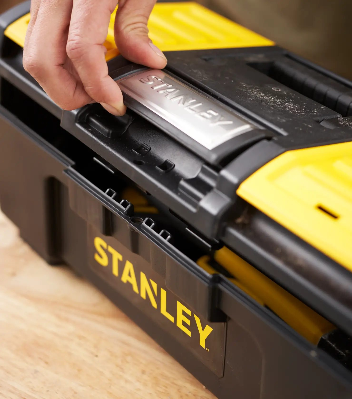 Photo of STANLEY 1-79-216 tool box in black and yellow, close-up of latch being opened on work surface.