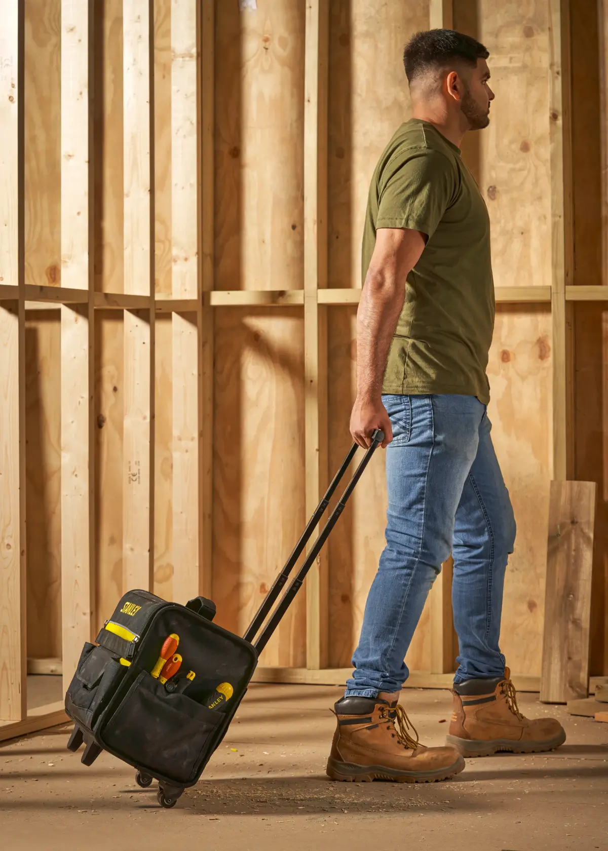 STANLEY 1-97-515 rolling tool bag with tools, carried by person in work boots at construction site.