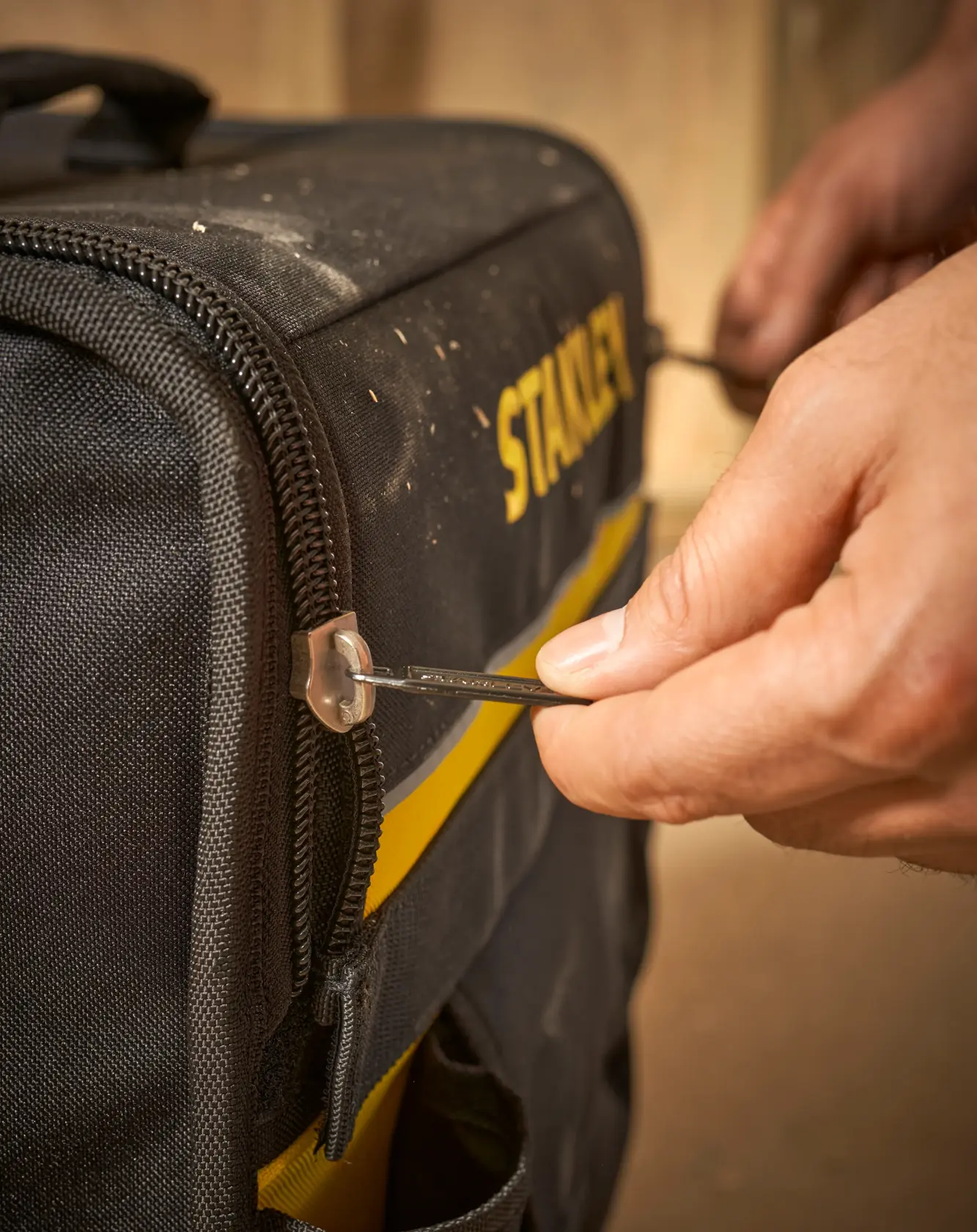 STANLEY 1-97-515 tool bag photography, close-up of hand using zipper on black and yellow fabric bag.