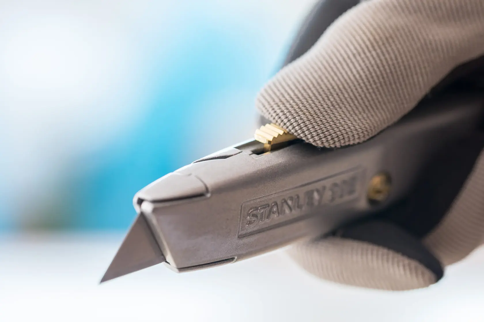 Close-up photo of STANLEY 2-10-099 utility knife held by gloved hand, showing metal body and exposed blade.
