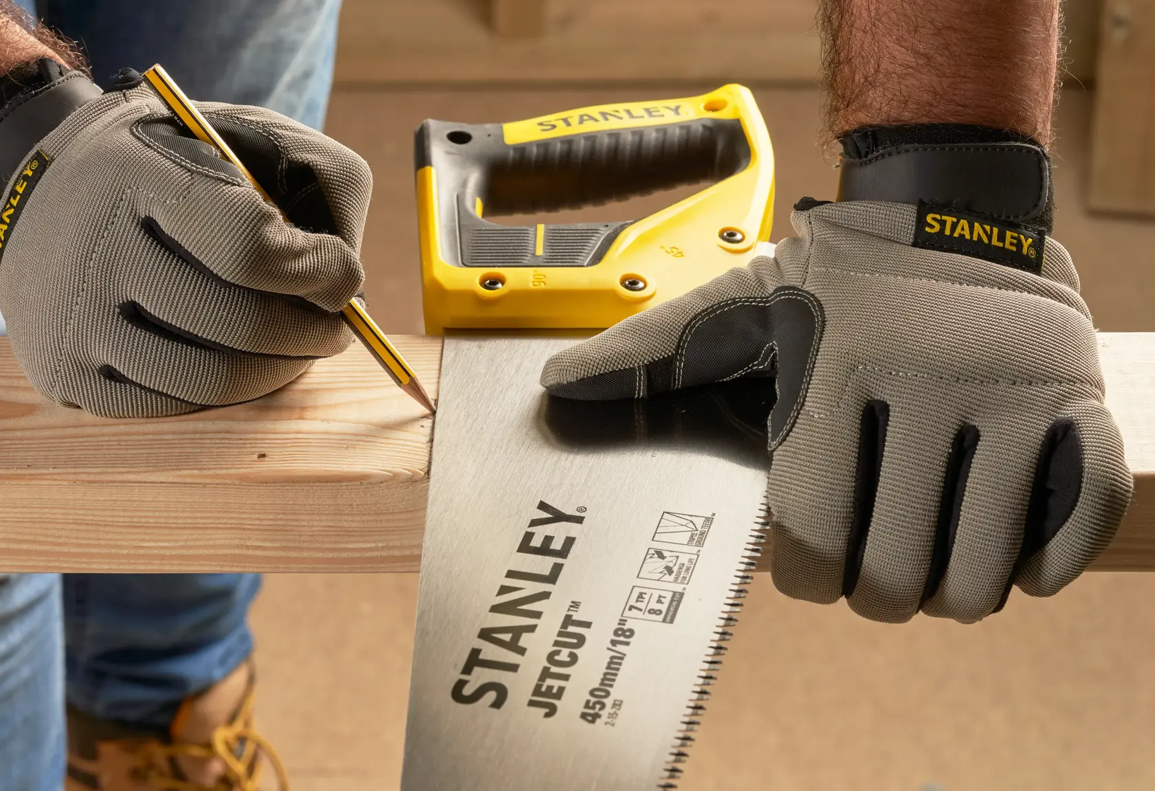 STANLEY 2-15-283 hand saw with yellow handle held by gloved hands, marking wood plank. Photography front angle.