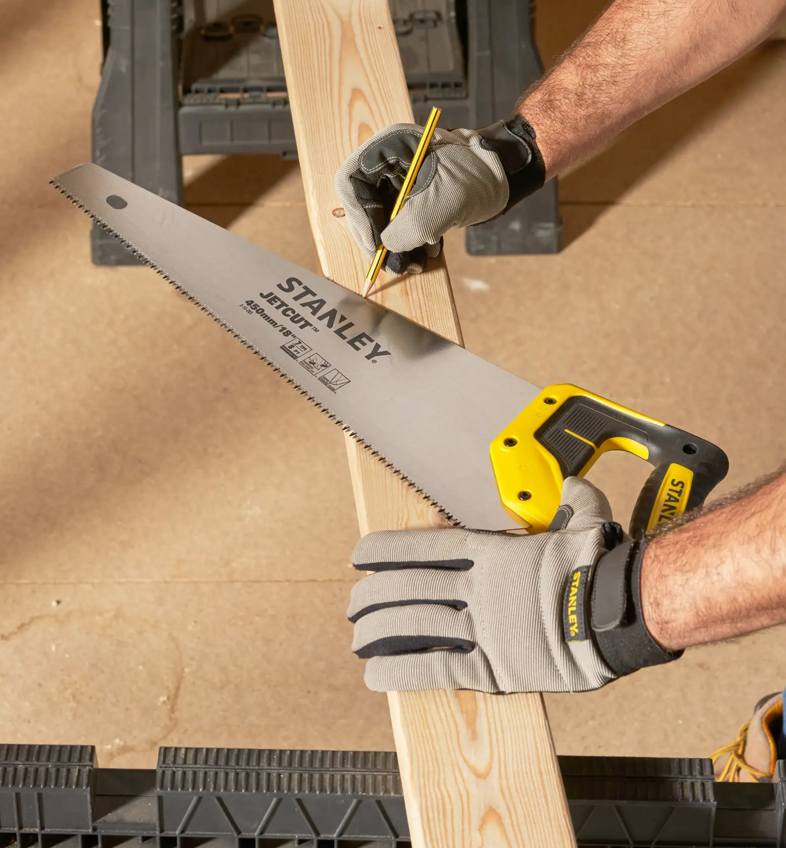STANLEY 2-15-283 hand saw with yellow handle held by gloved hand marking wood plank, angled view.