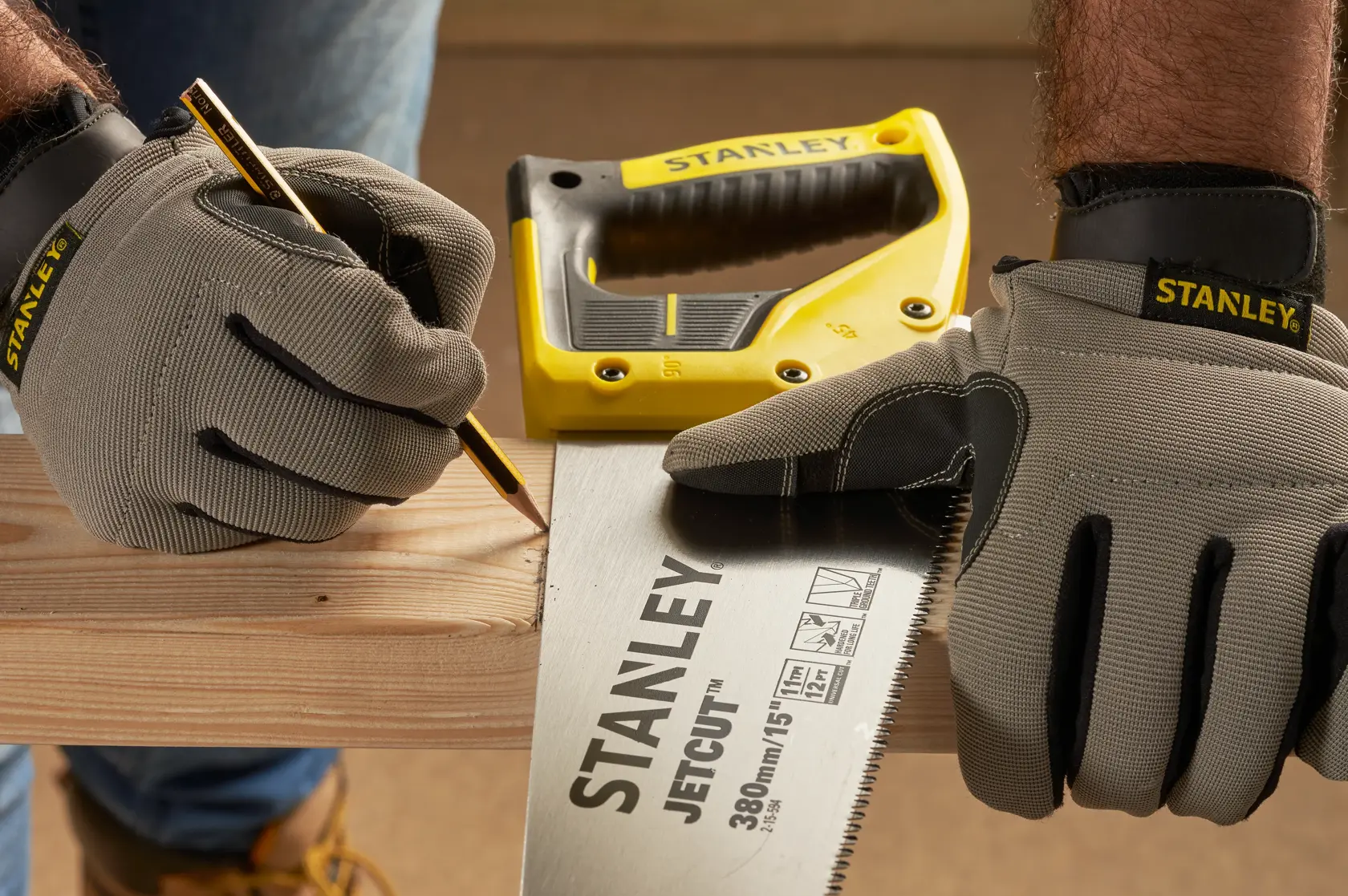 STANLEY 2-15-594 hand saw in use, gloved hands marking wood, pencil and yellow handle visible.