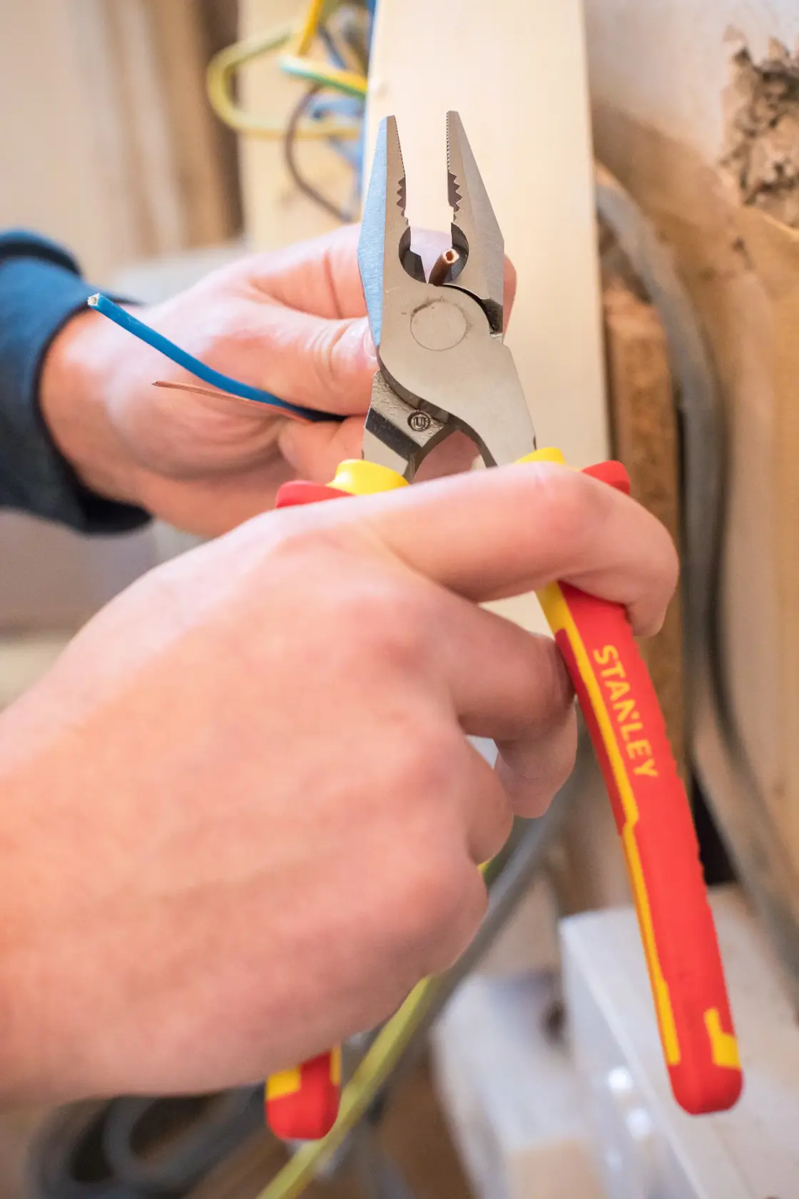 STANLEY 84-002-S pliers with red and yellow handles gripping a blue wire during electrical work.
