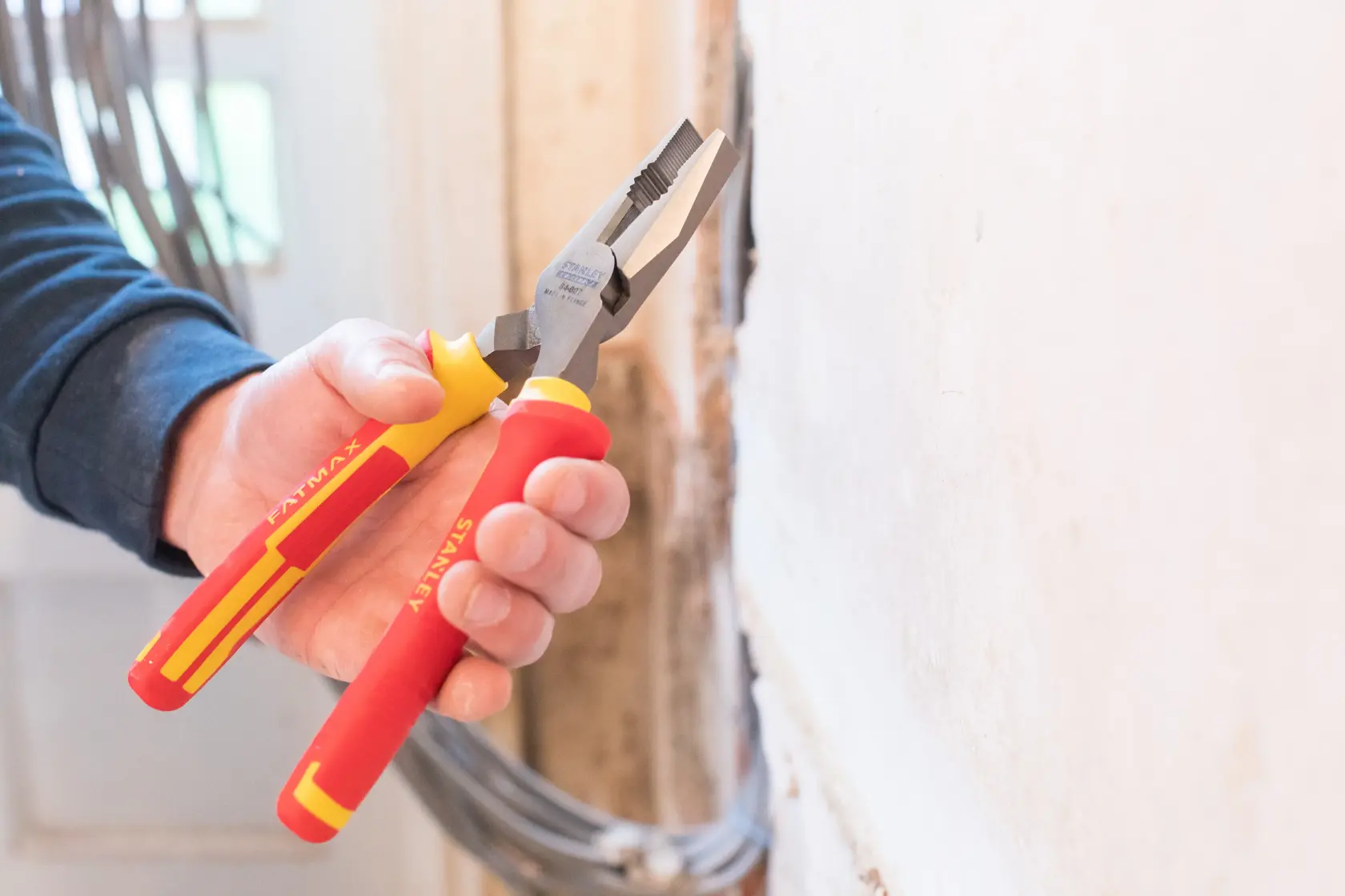 Photo of STANLEY 84-002-S insulated combination pliers with red and yellow handles in use near wall.