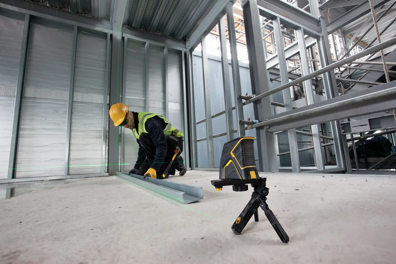 STANLEY FMHT1-77348 laser level on tripod at construction site, worker aligns metal beam using green laser lines.