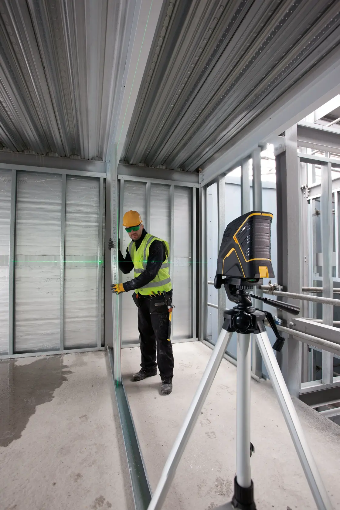 STANLEY FMHT1-77348 laser level on tripod used at construction site, worker aligns metal framing.