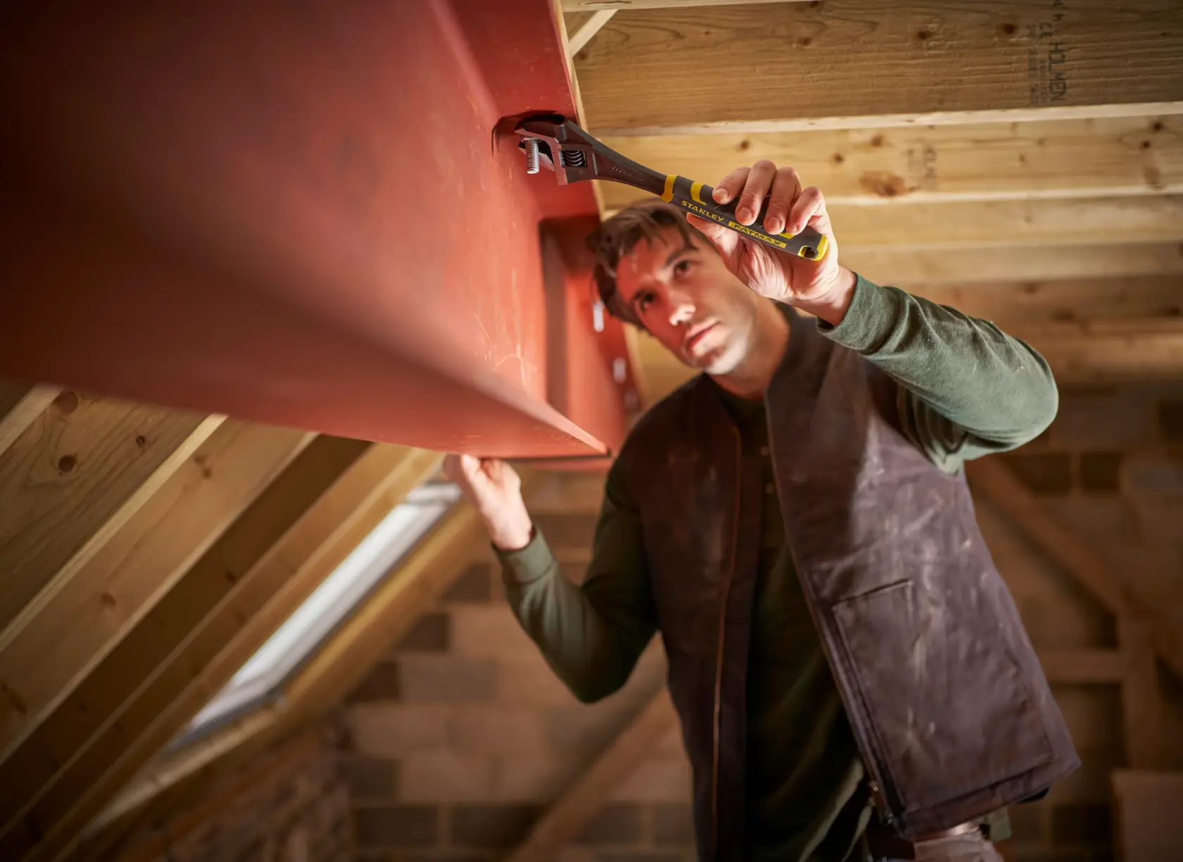 STANLEY FMHT13128-0 adjustable wrench used by a worker on a red steel beam in an attic space.