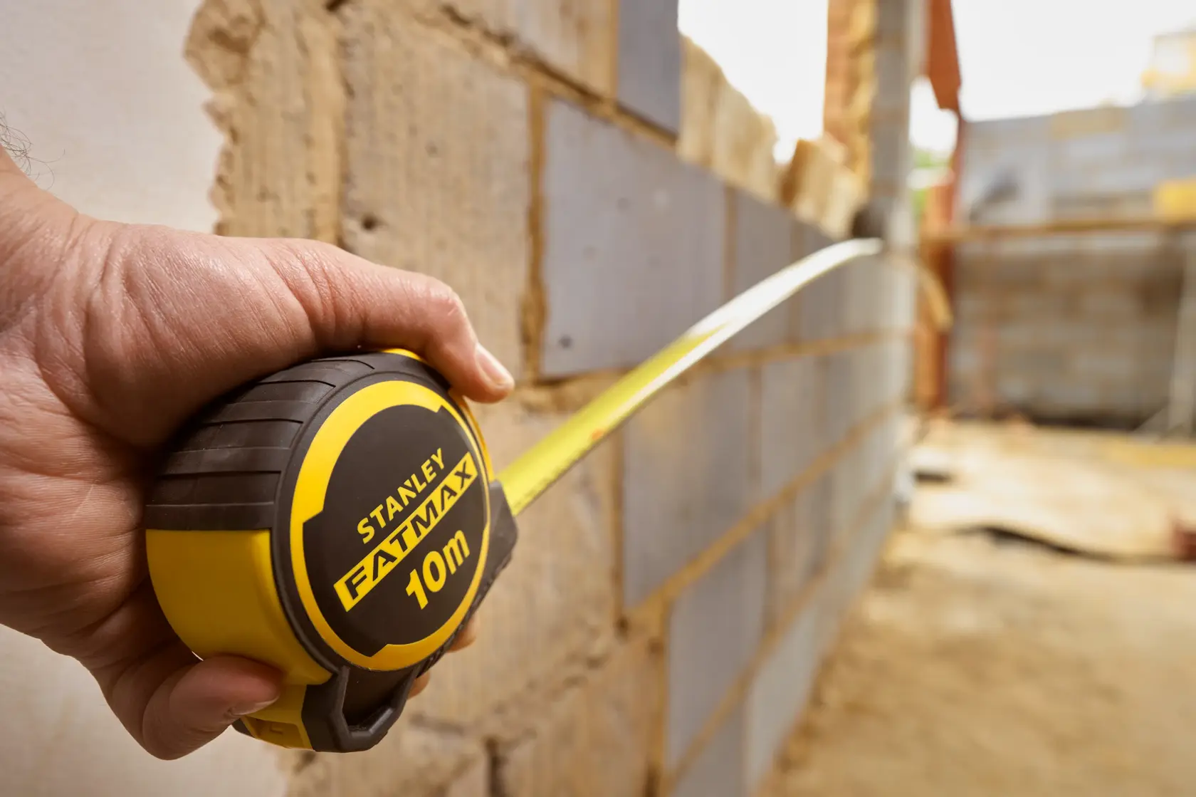 Photo of STANLEY FMHT33010-3 FATMAX 10m tape measure held against a brick wall at a construction site.