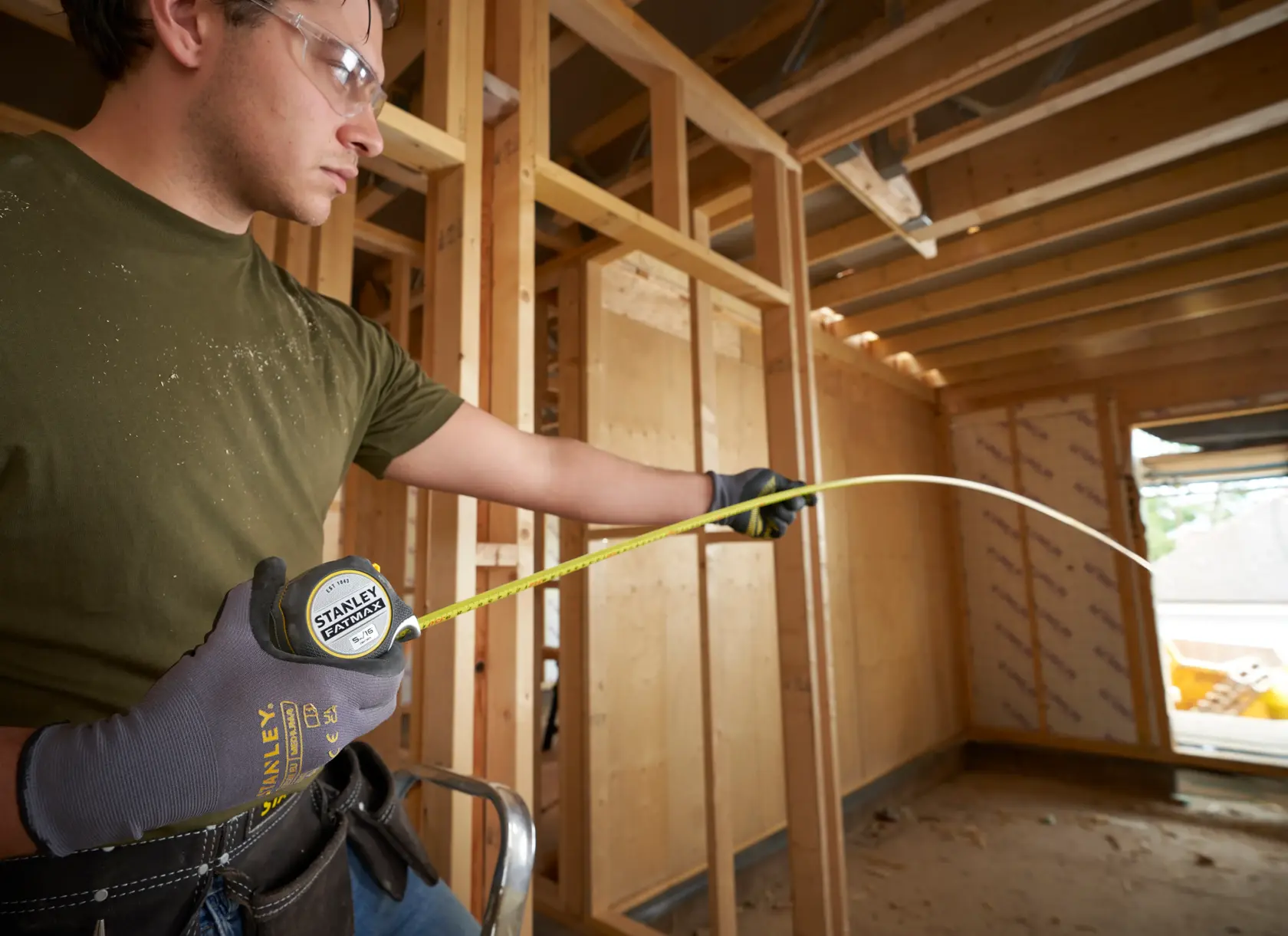 Photo of STANLEY FMHT38215-5 tape measure extended by worker wearing gloves, measuring in a building under construction.