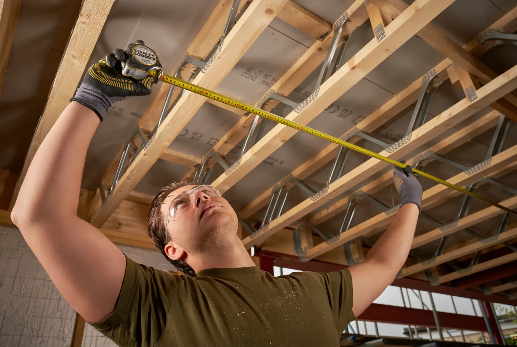 Photo of STANLEY FMHT38215-5 tape measure used by a person measuring wooden beams indoors.