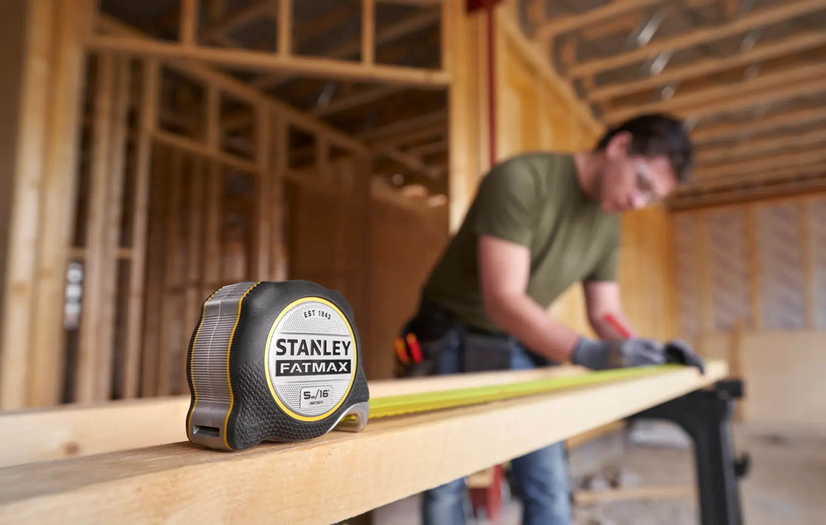 Photo of STANLEY FMHT38215-5 tape measure on wood in construction site, person measuring in background.
