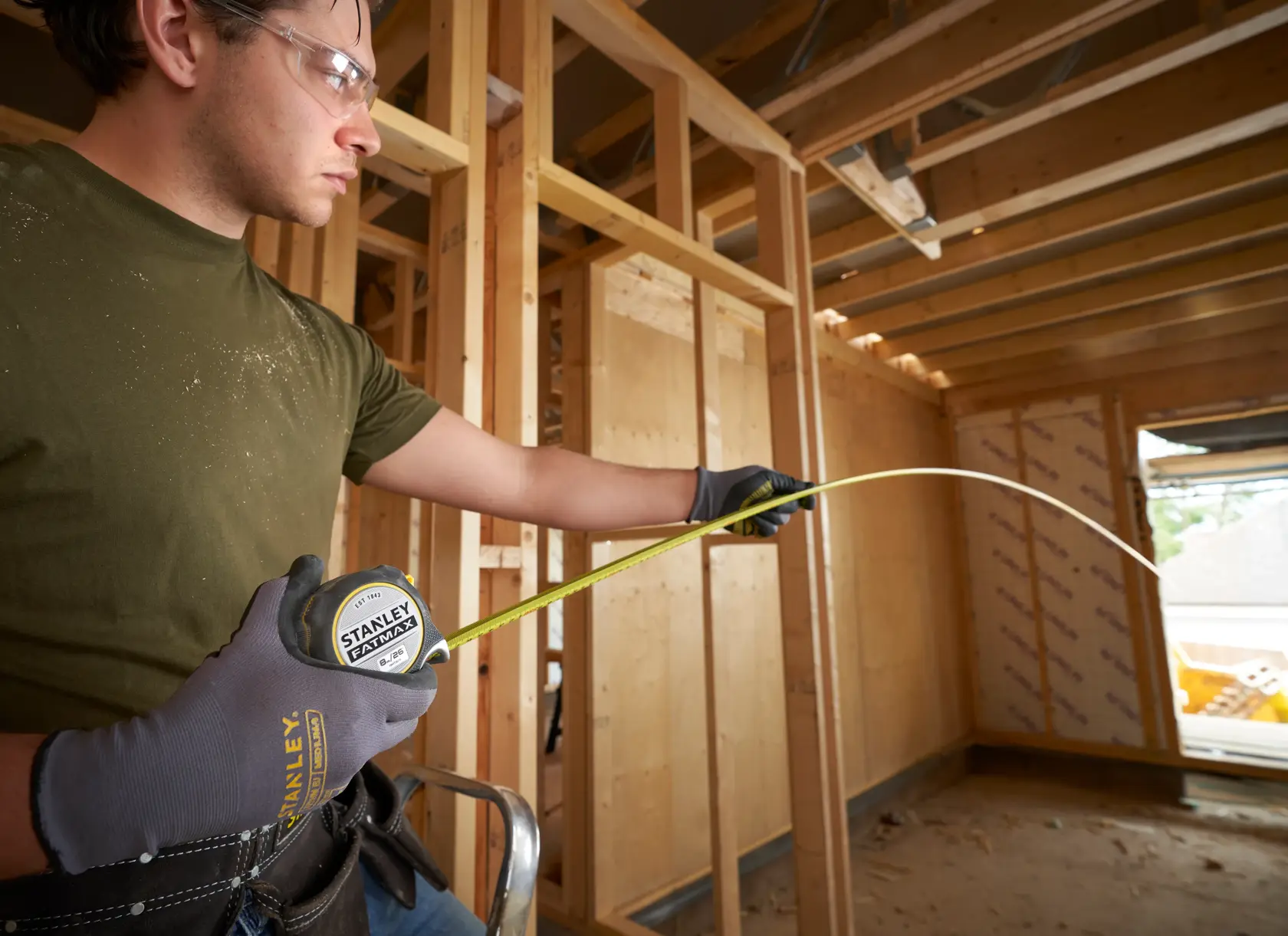 Photo of STANLEY FMHT38218-5 tape measure extended by gloved hand on construction site framework.