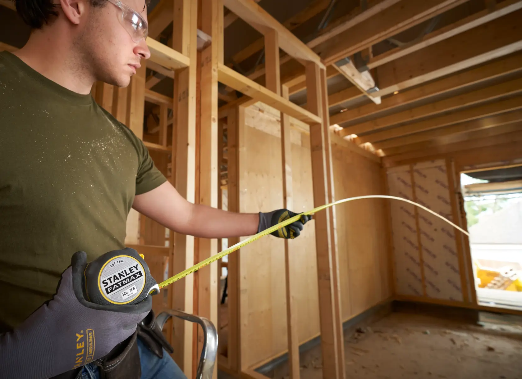 STANLEY FMHT38233-5 tape measure extended by worker in gloves at a wooden construction site.