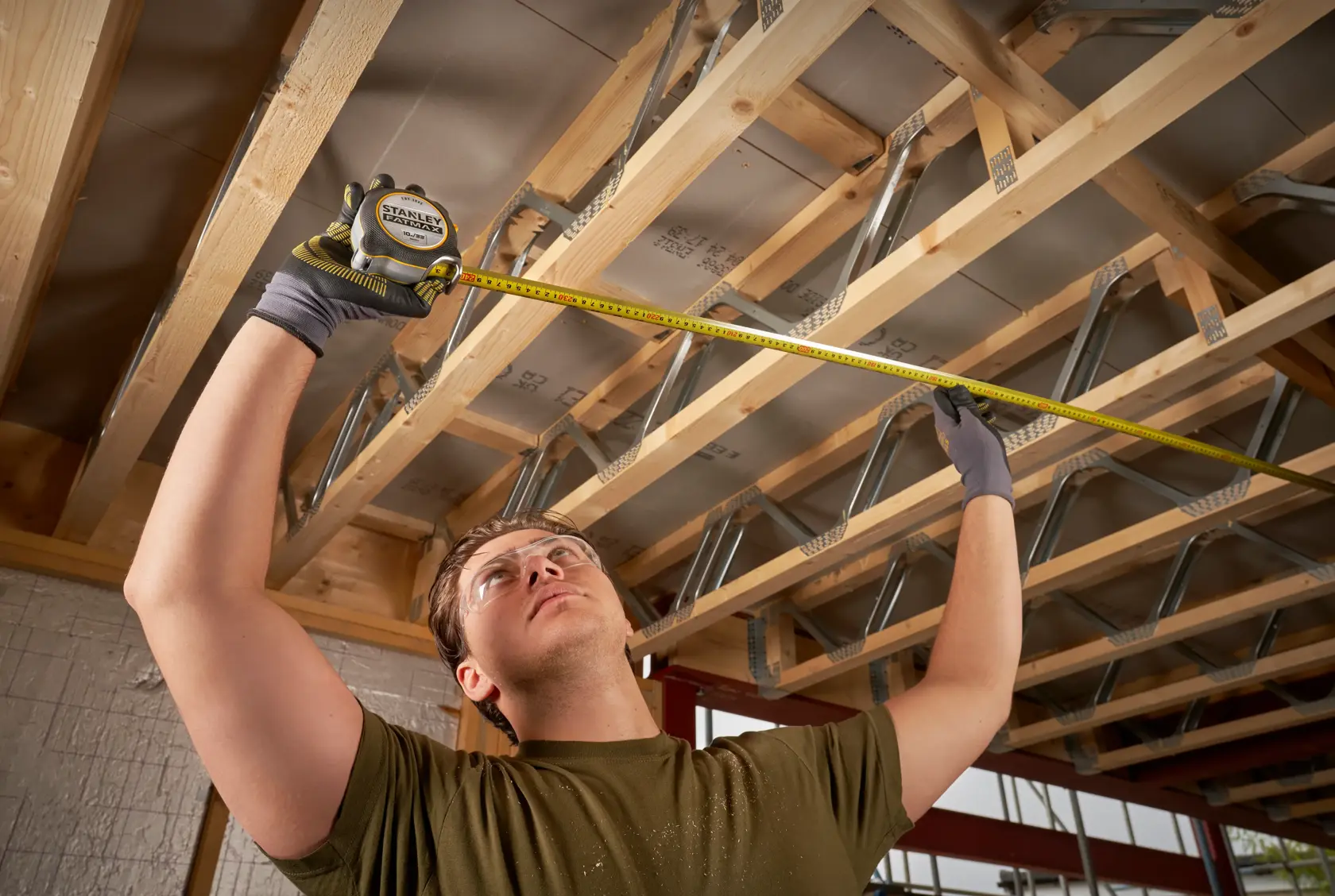 STANLEY FMHT38233-5 tape measure used by a person measuring wooden beams in a construction setting.