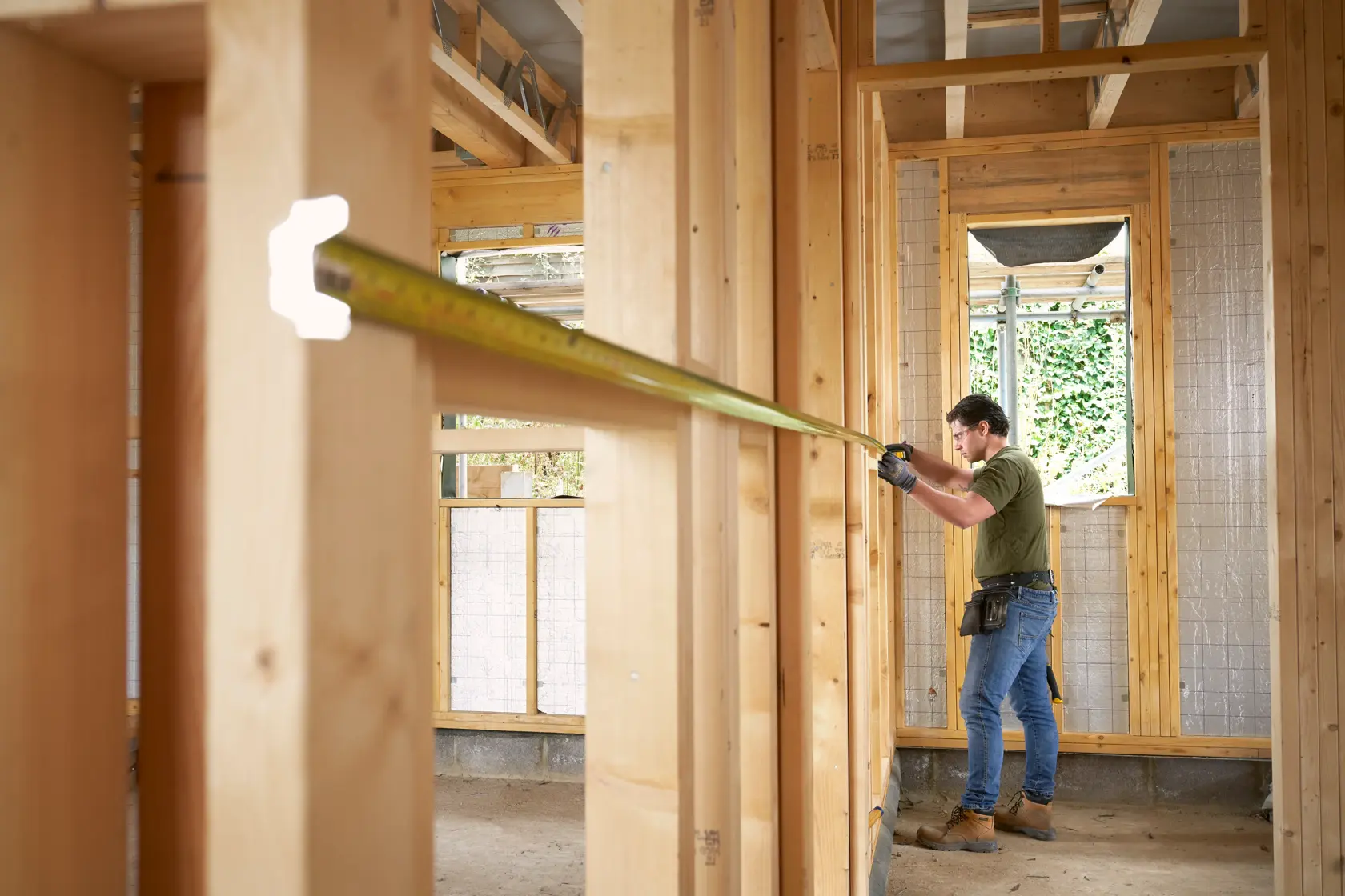 STANLEY FMHT38233-5 tape measure in use on a construction site, worker measuring wooden wall framing.