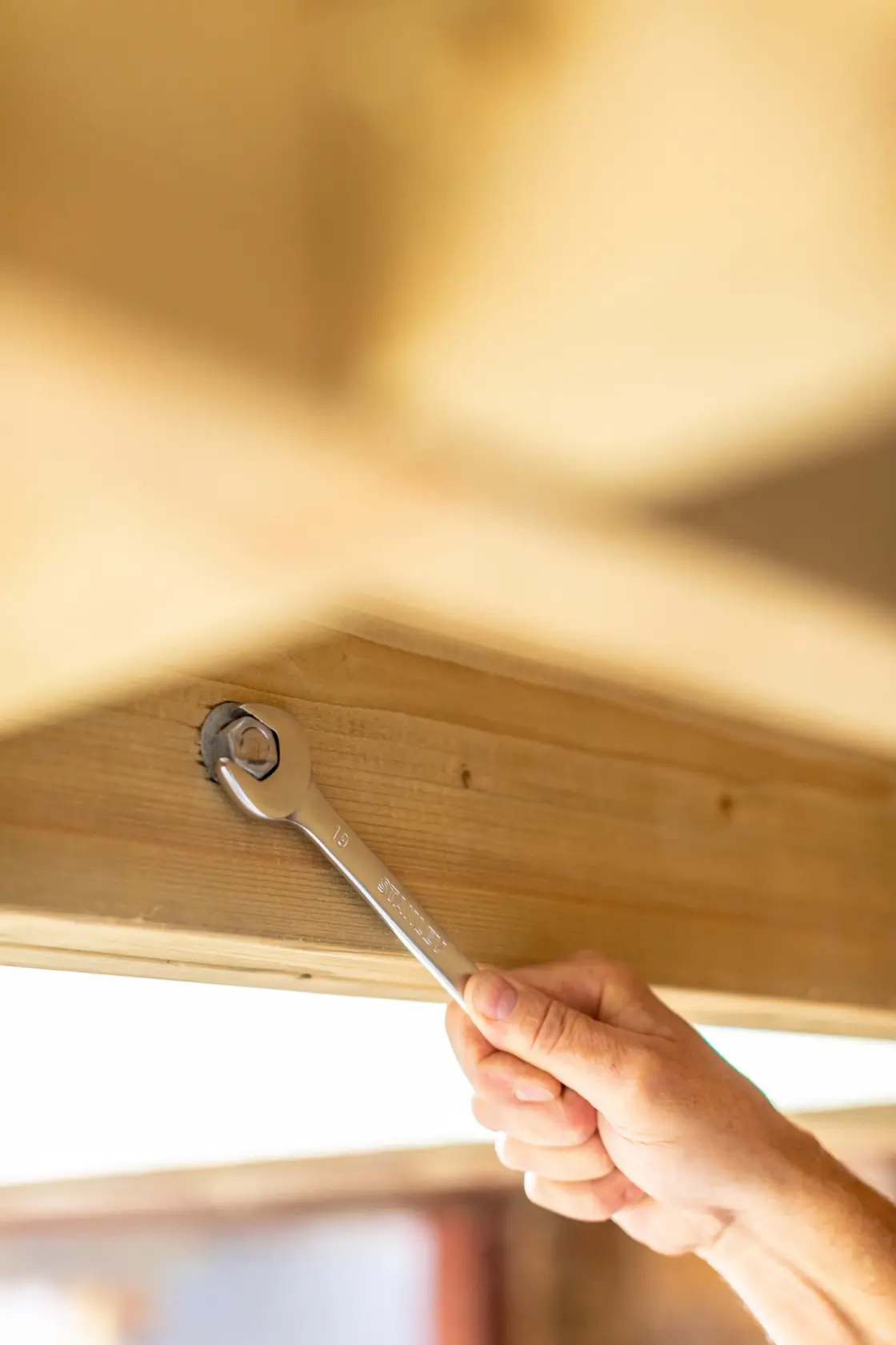 STANLEY FMMT82844-0 combination wrench used on a bolt in a wooden beam, close-up action shot.
