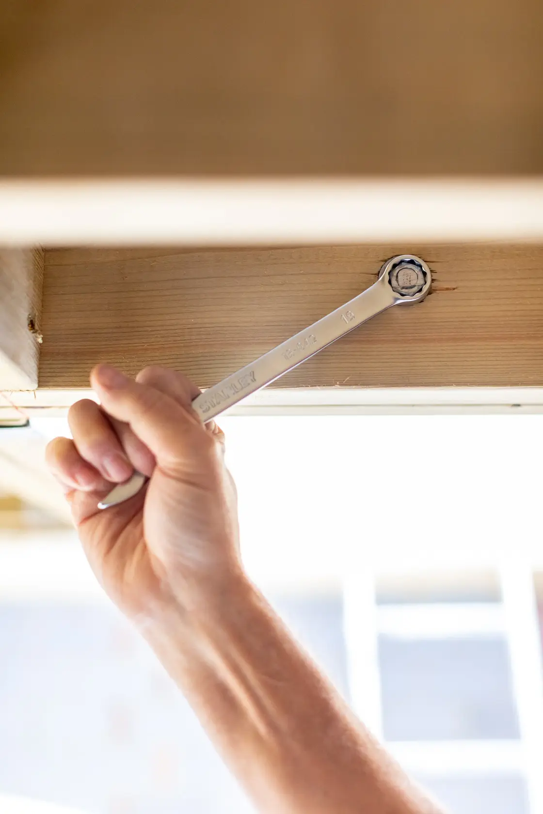 Photo of hand using STANLEY FMMT82844-0 combination wrench on bolt under wooden surface.