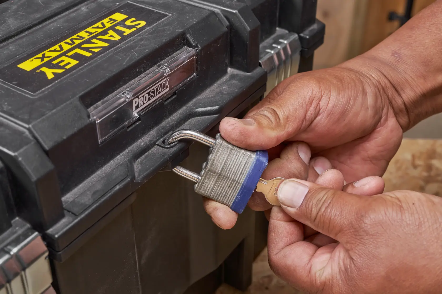 STANLEY FMST1-71971 toolbox secured with padlock, key held in hand, close-up photography.