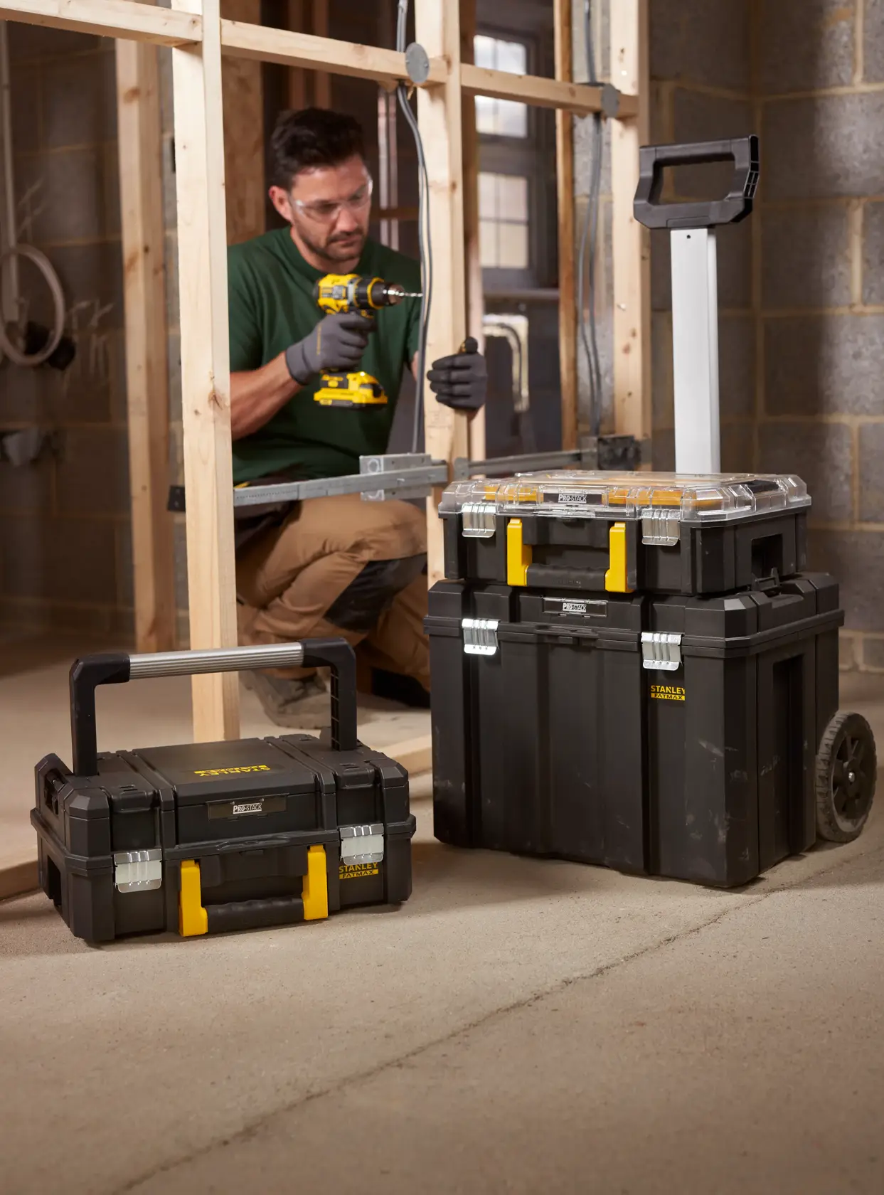 STANLEY FMST1-80103 stackable black toolboxes with yellow latches and wheeled trolley, shown on a construction site.