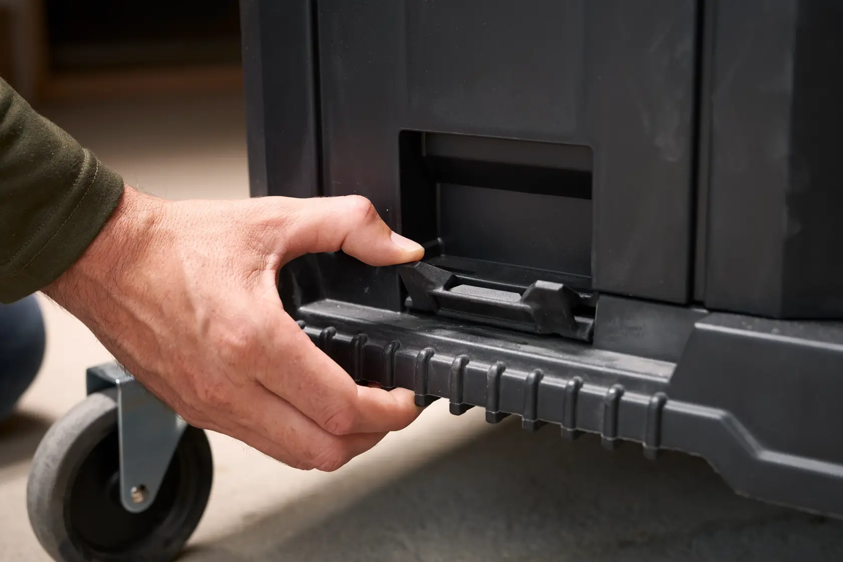Photo of a hand operating the latch on a black STANLEY FMST1-80107 rolling toolbox, close-up view.