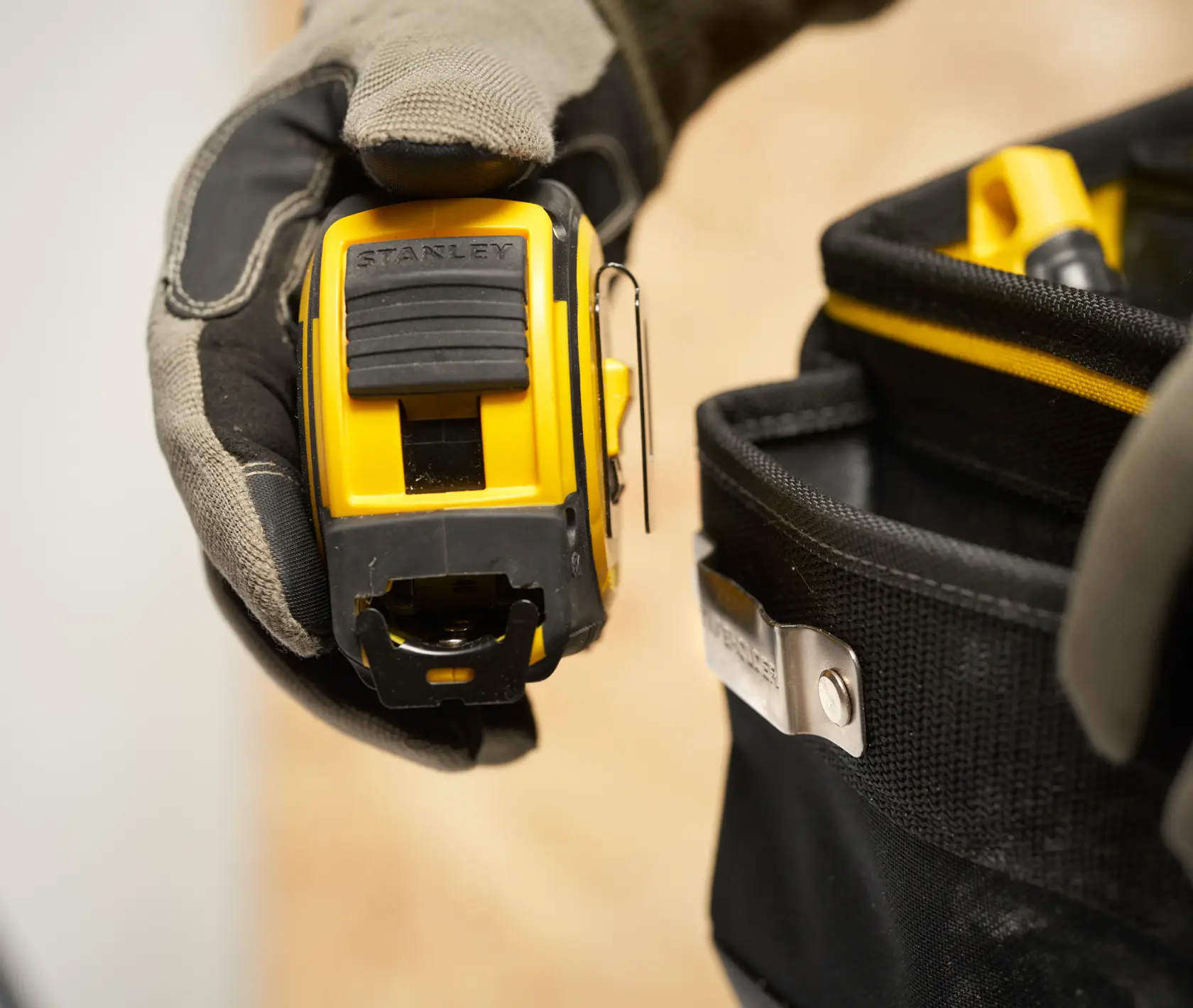 Photo of STANLEY FMST17624-1 tape measure held by a glove with a tool belt in view.