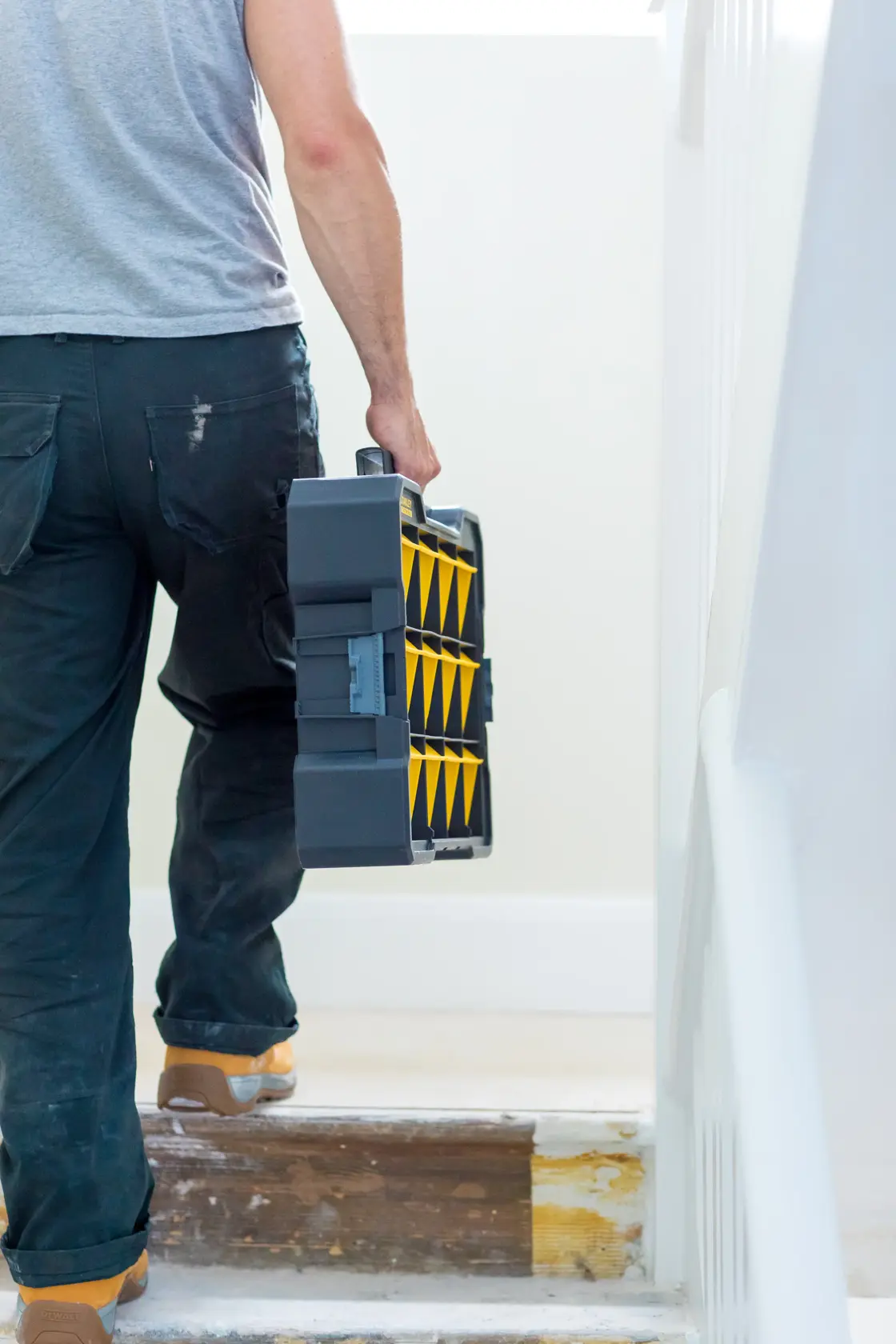 Photo of a person carrying a STANLEY FMST81077-1 tool organizer with yellow compartments up stairs.