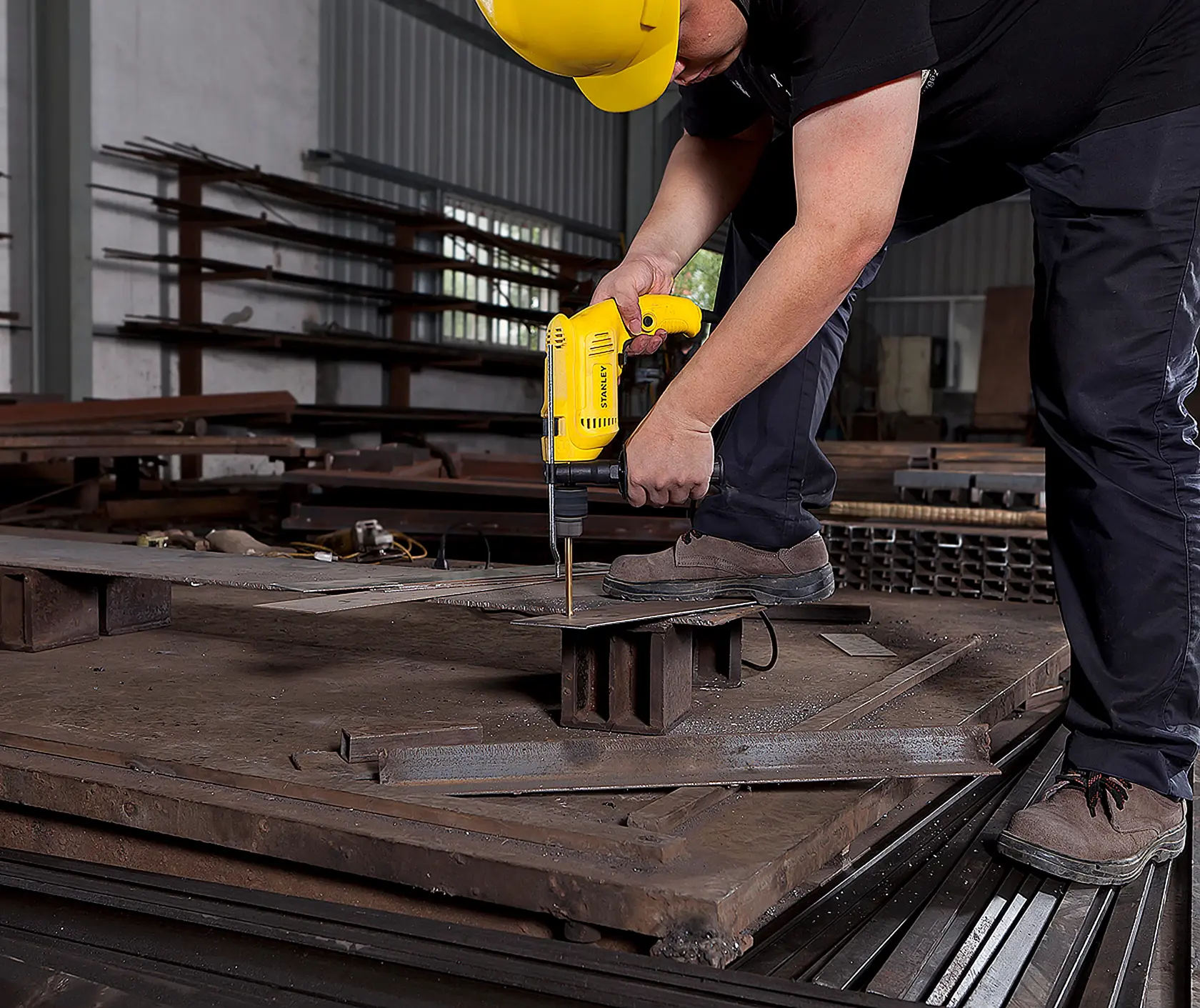 STANLEY SDH600 yellow drill being used to drill metal sheet in industrial workshop, side angle.