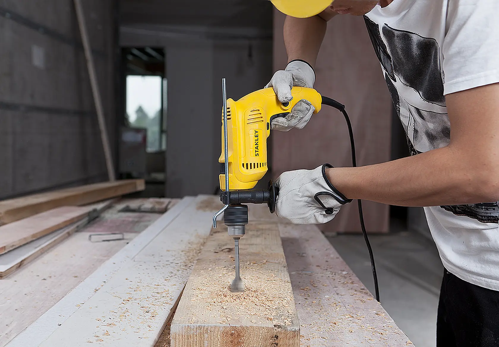 Photo of a worker using a STANLEY SDH600 corded drill to bore a hole in a wooden plank in a workshop.