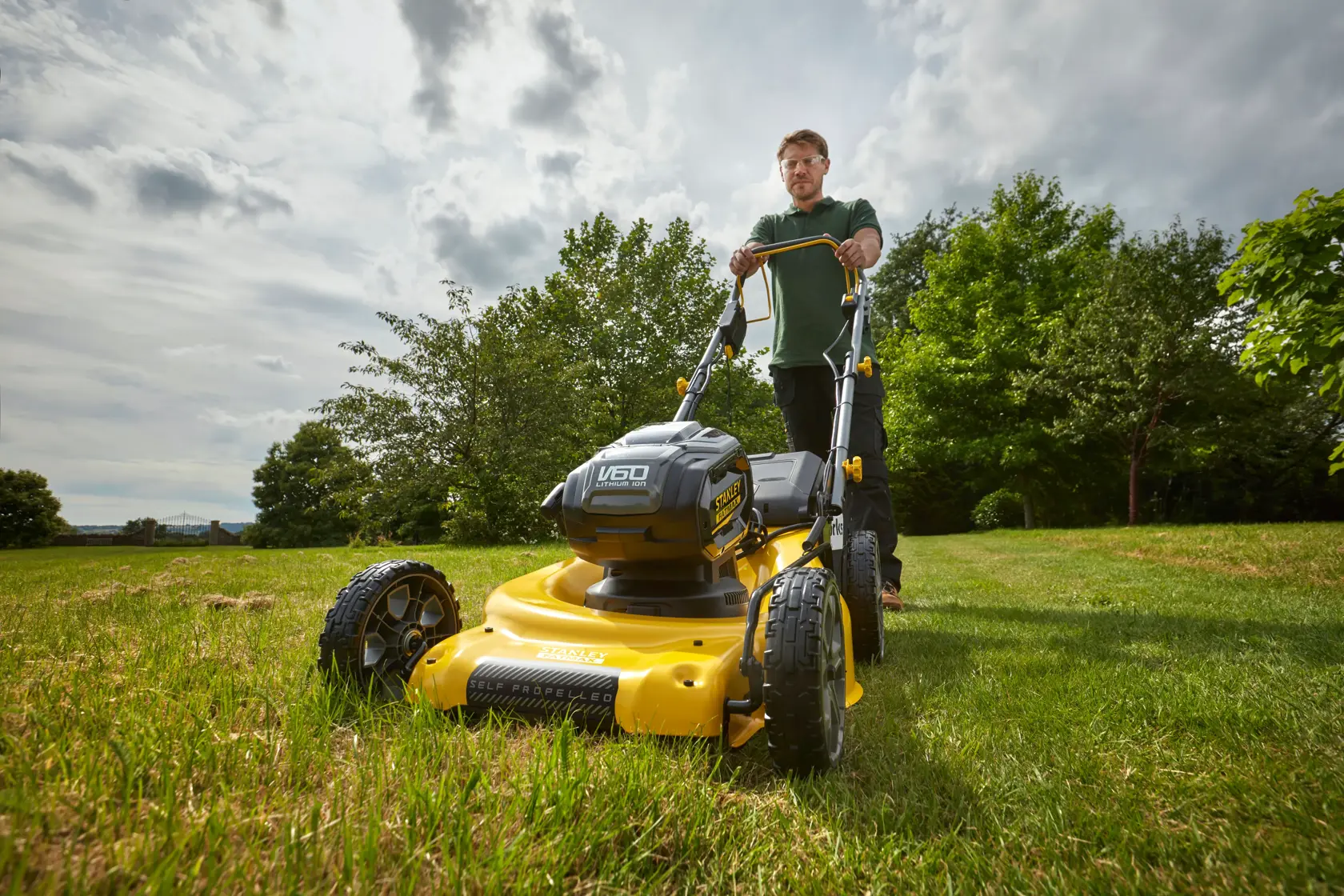 Photo of STANLEY SFMCMS2653B yellow cordless lawn mower in use on grass, front angle outdoors.