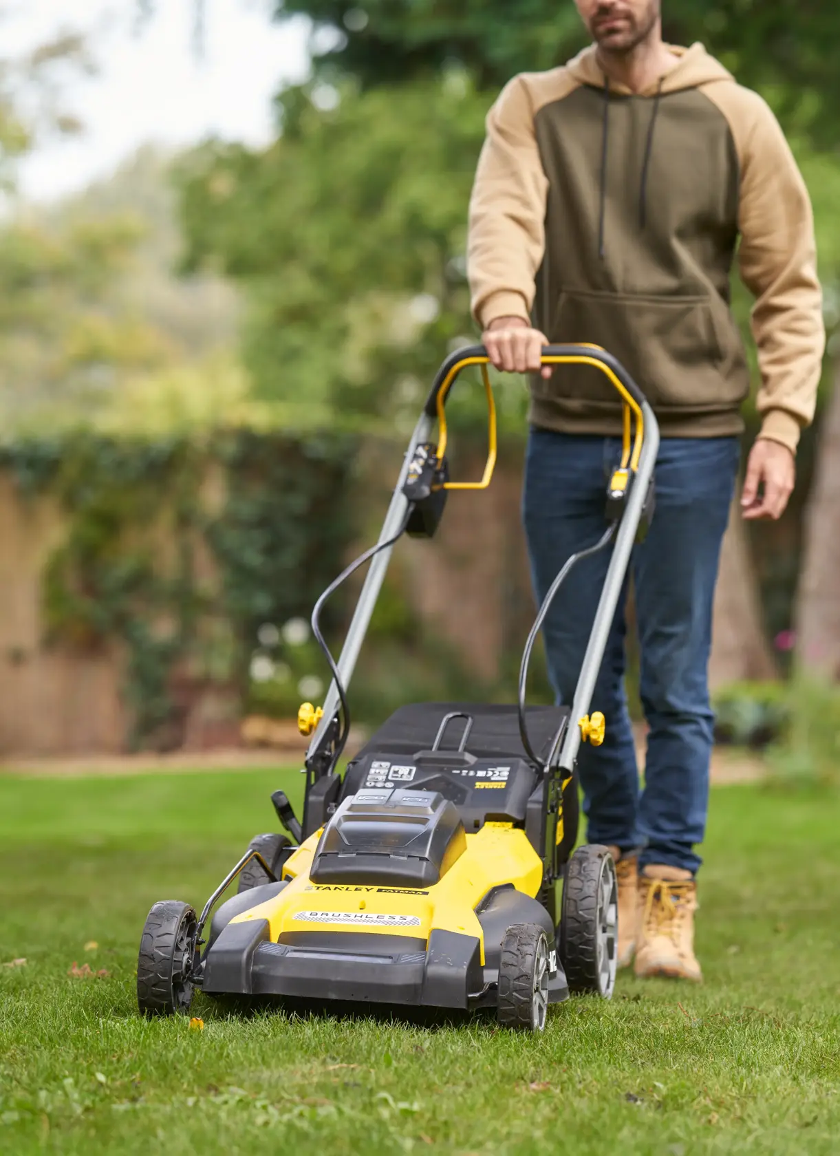 Photo of STANLEY SFMCMWS251B lawn mower in use outdoors, yellow and black design, front angle view.