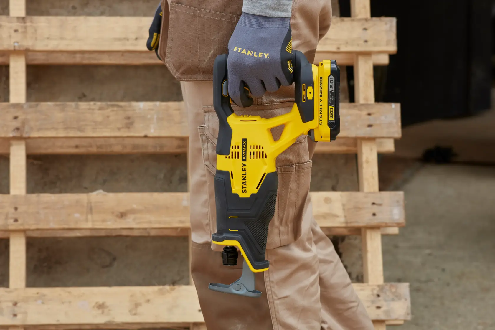 Stanley SFMCS300D1K yellow and black reciprocating saw held by gloved hand, shown outdoors near wooden pallets.