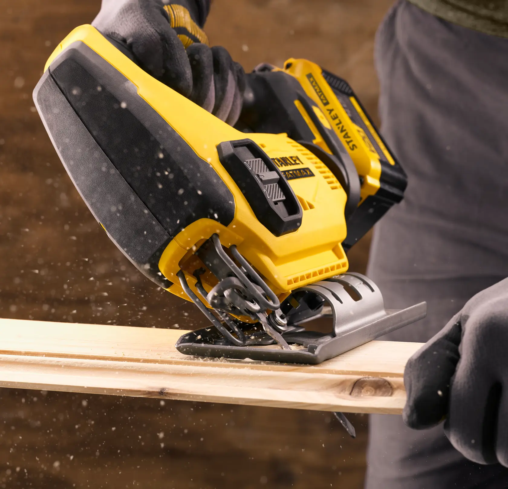 Stanley cordless jigsaw cutting wood, sawdust visible, held by gloved hands.