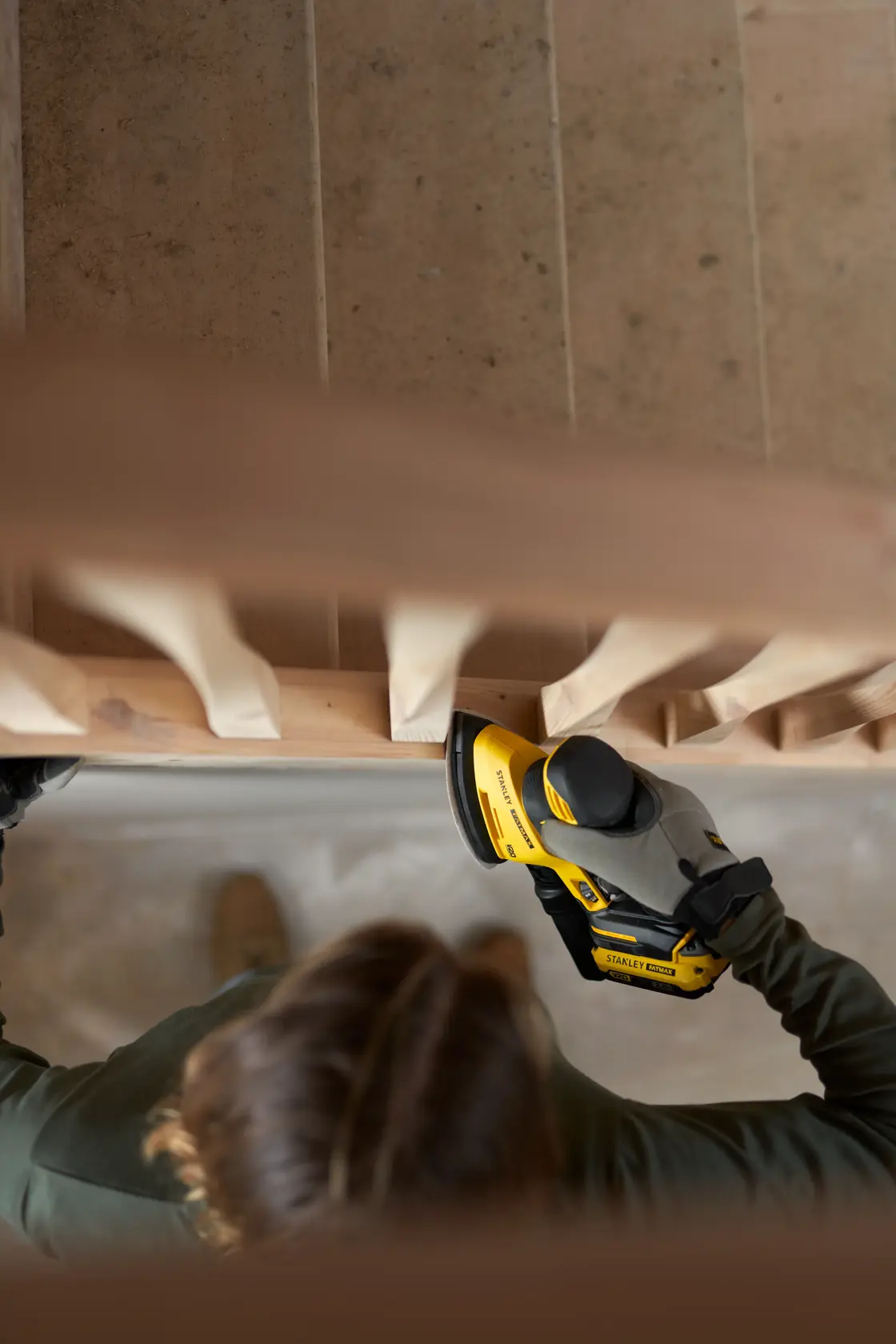 Photo of STANLEY SFMCW221D1S sander being used on a wooden stair railing from overhead.