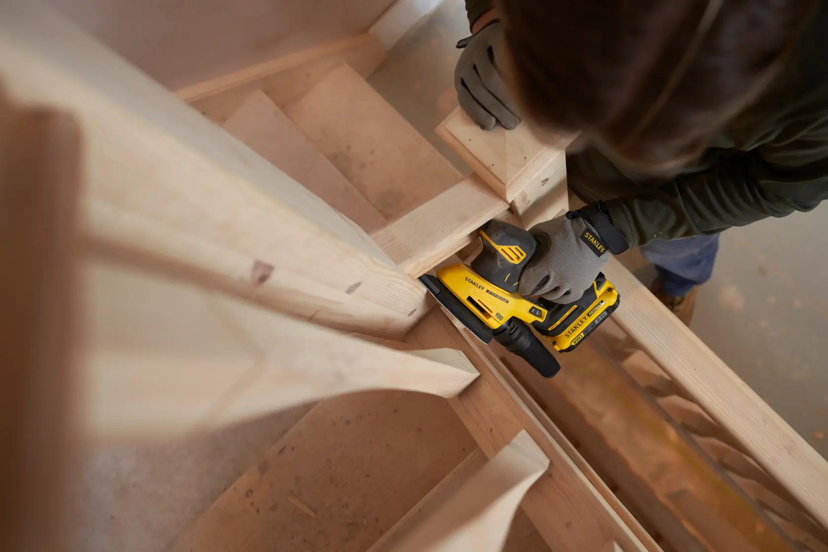 STANLEY SFMCW221D1S cordless sander used on wooden stairs, shown in action from above.