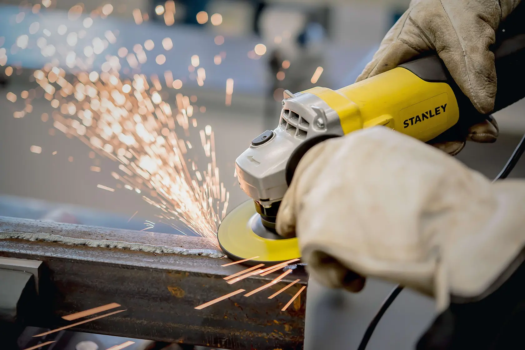 Photo of STANLEY STA0413 angle grinder in use, grinding metal with visible sparks, operated by gloved hands.