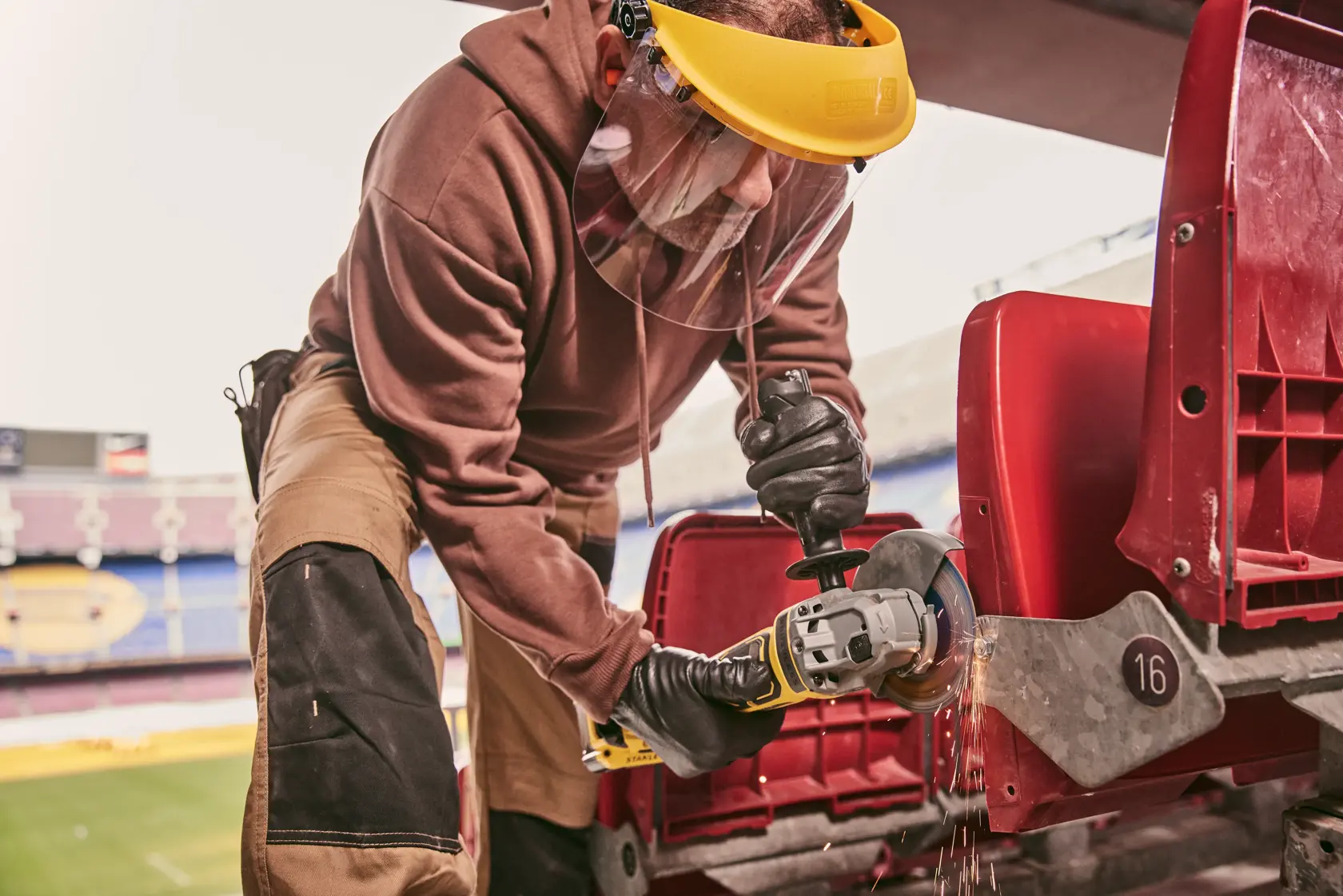 STANLEY STA32637 angle grinder in use cutting metal stadium seat armrest, close-up action shot.