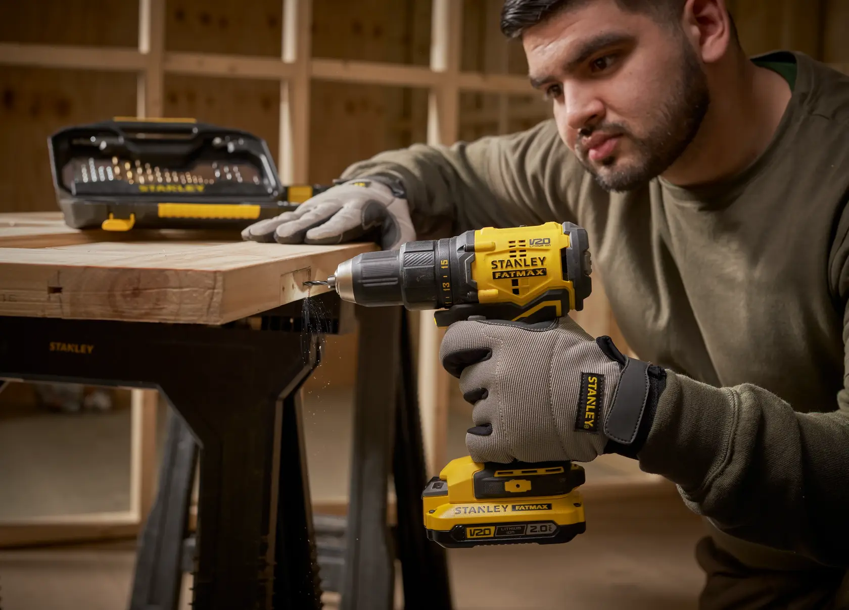 STANLEY STA7184 cordless drill in use on wood, drill bit set visible, workshop background.