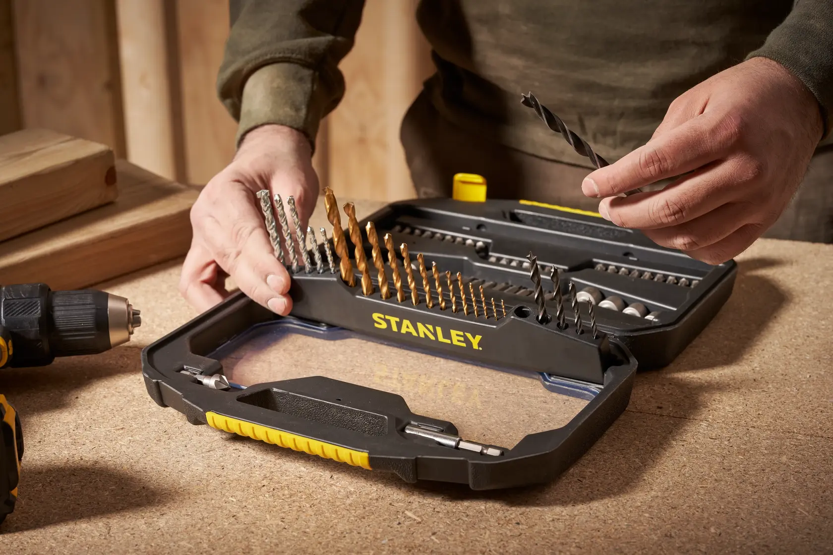 STANLEY STA7184 drill bit set in black case on workbench, hand selecting a drill bit, workshop background.